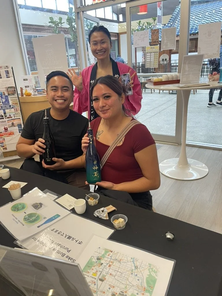 Photo of a couple holding two of the sake tasting bottles with the Sake Trend expert behind them.