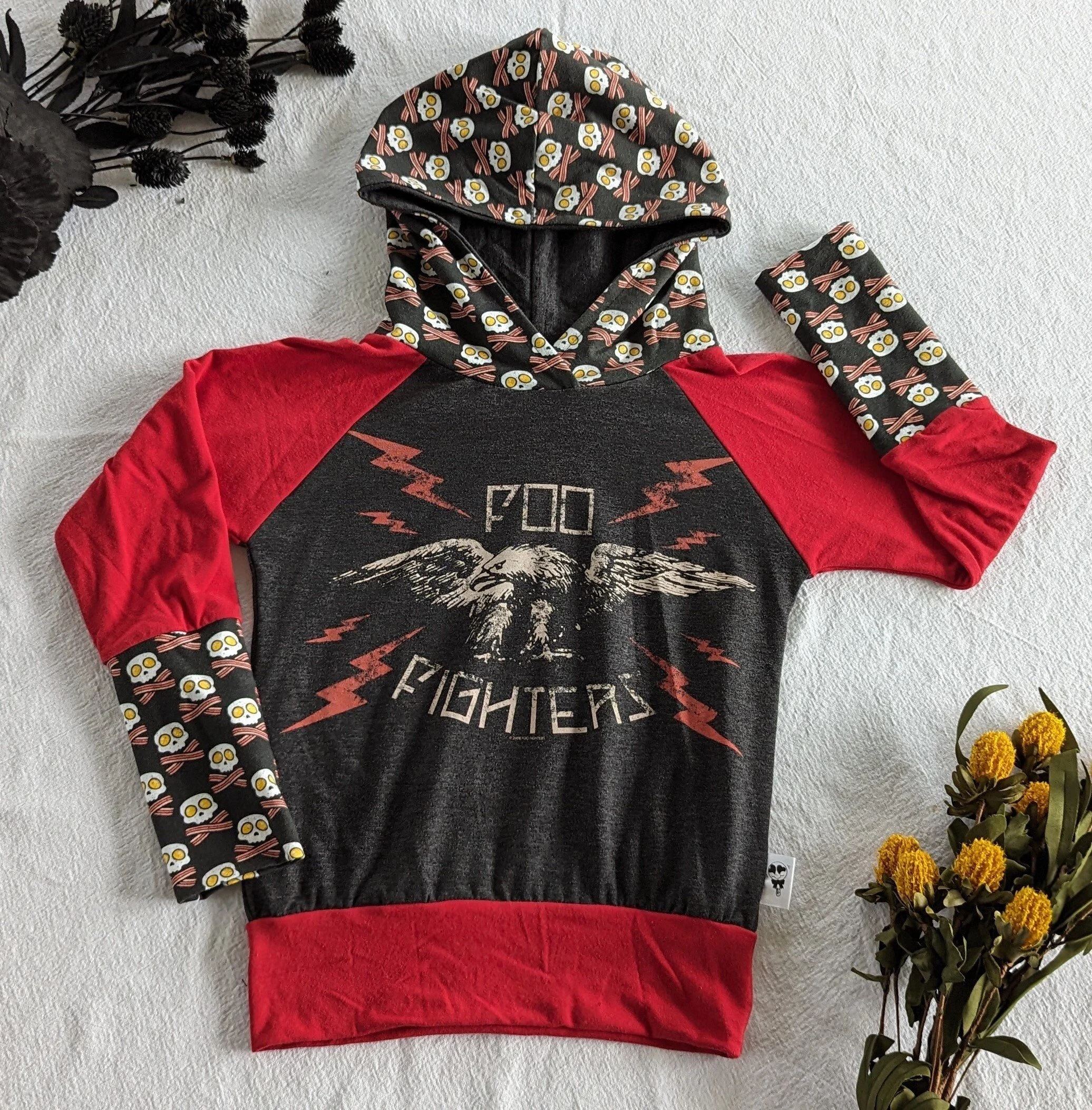 A dark grey children's hoodie with red sleeves and waistband, hood and sleeves have egg and bacon skull and cross bone pattern, featuring an eagle, lightning bolts, and the words 'FOO FIGHTERS' on front of torso