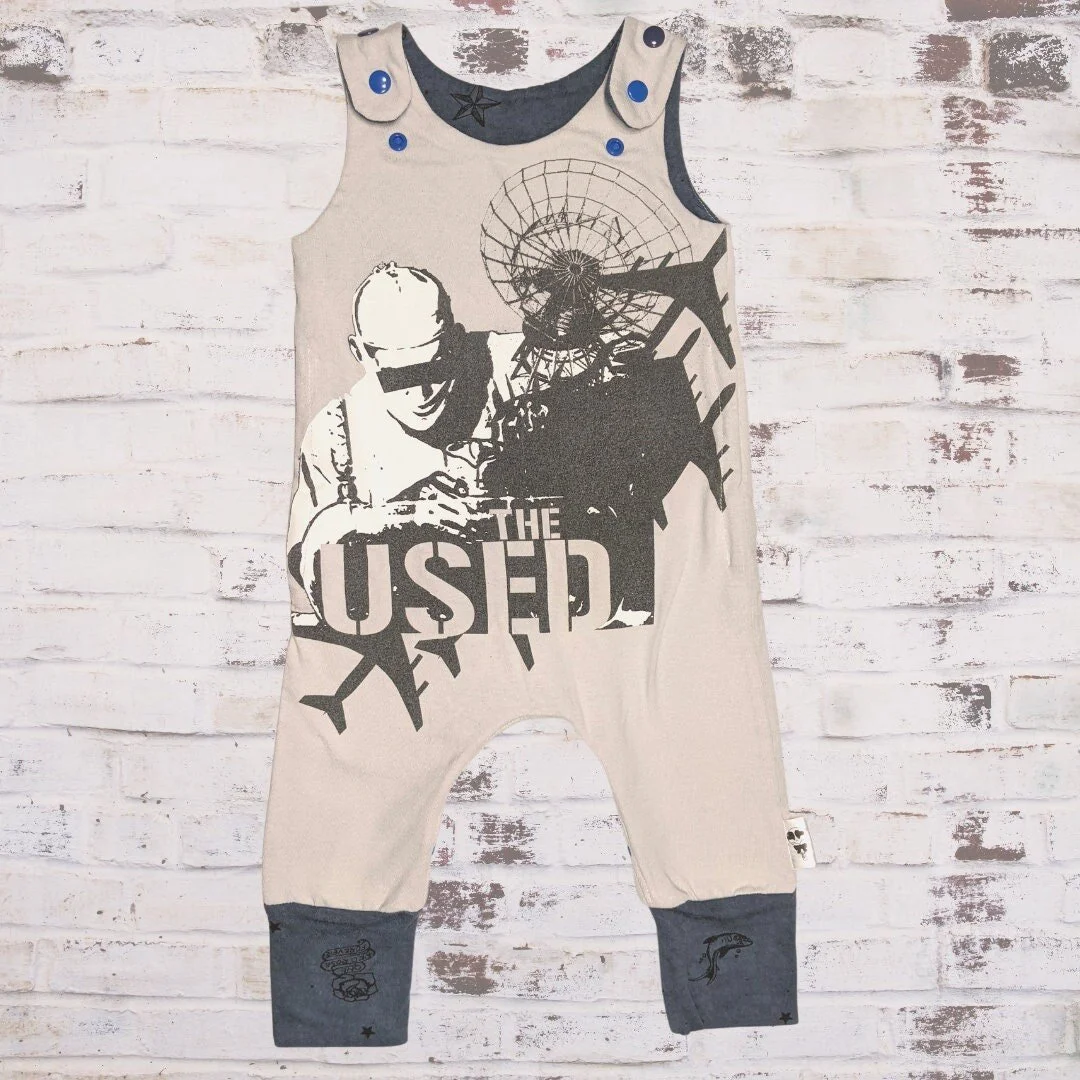 A sleeveless R$H branded baby romper with black graphic print of a person with outdoor gear and a Ferris wheel, against a white brick wall background.