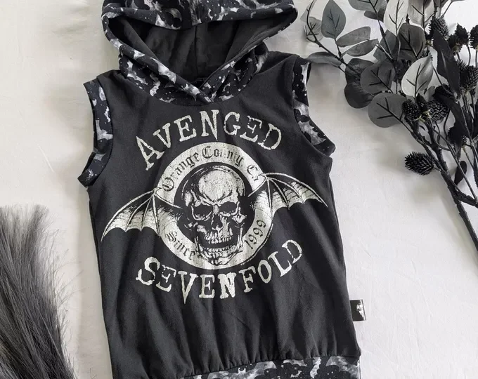 Black sleeveless hoodie with a skull and bat wings graphic and the words "Avenged Sevenfold" on the front, surrounded by leaves and fabric elements.