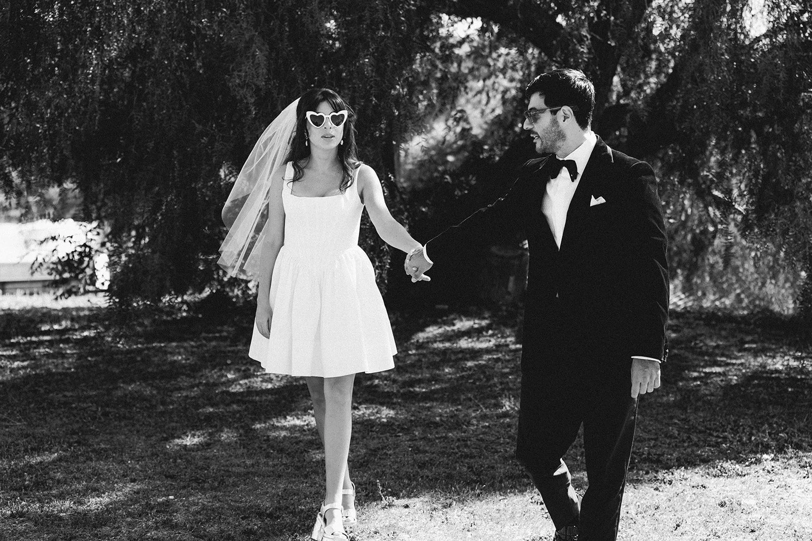 A black-and-white photo of a bride and groom standing closely together against a textured stone wall, with the bride holding a bouquet and both looking at each other.