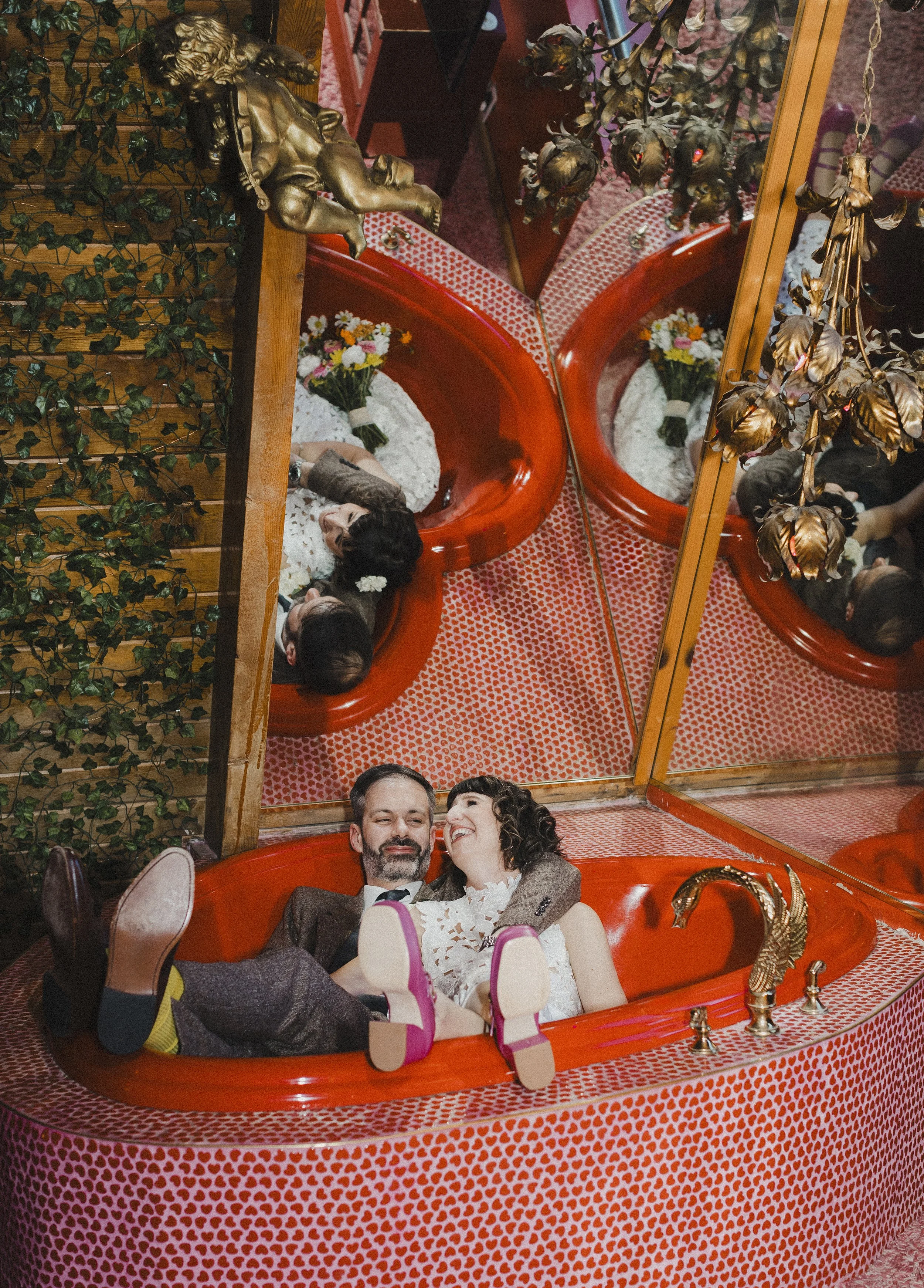 A couple in wedding attire sharing a kiss inside a red heart-shaped love lock with a patterned pink background.