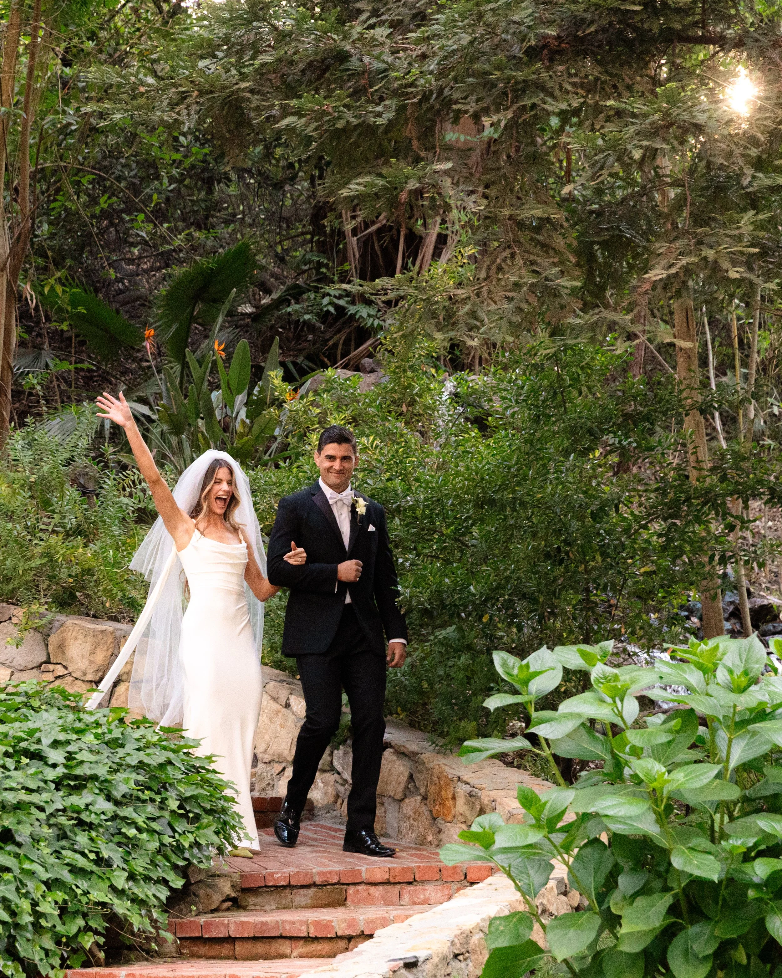 Bride and groom walking down brick steps in a lush garden, celebrating their wedding.