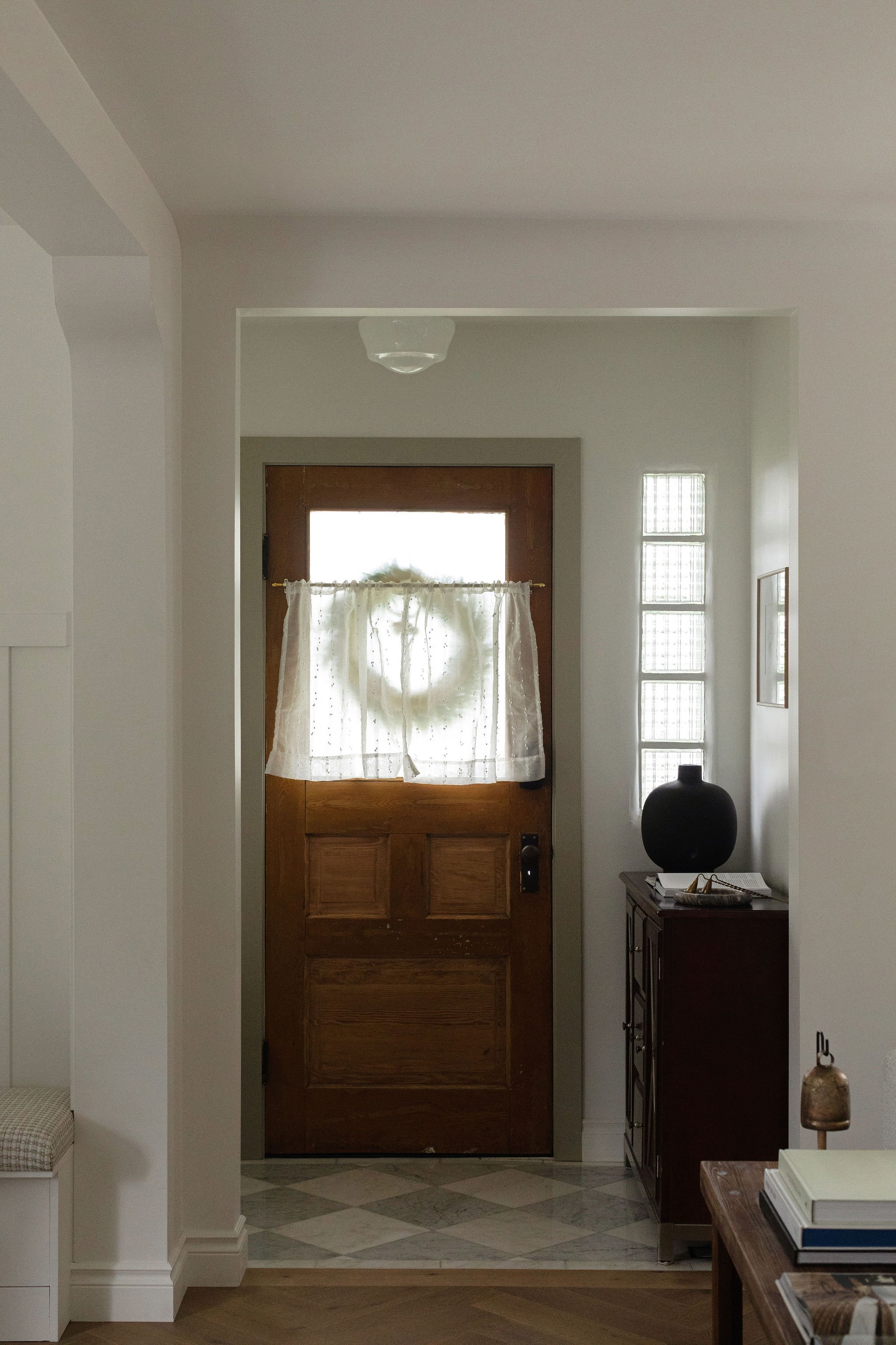 Cottage entryway featuring a traditional wood front door, patterned tile flooring and vintage-inspired furnishings.
