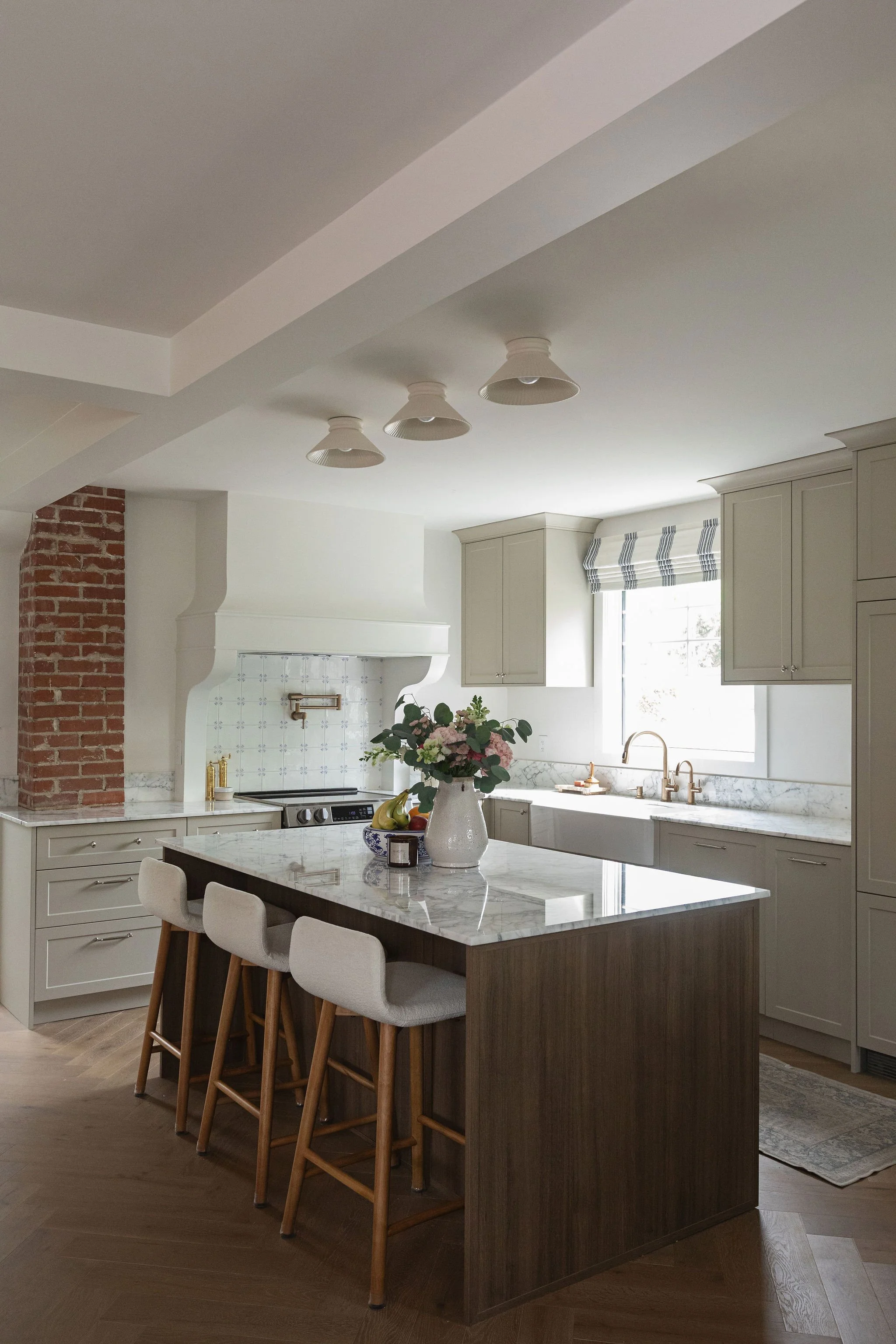 Custom dark wood kitchen island with Gioia marble counters, upholstered stools and warm beige cabinetry.