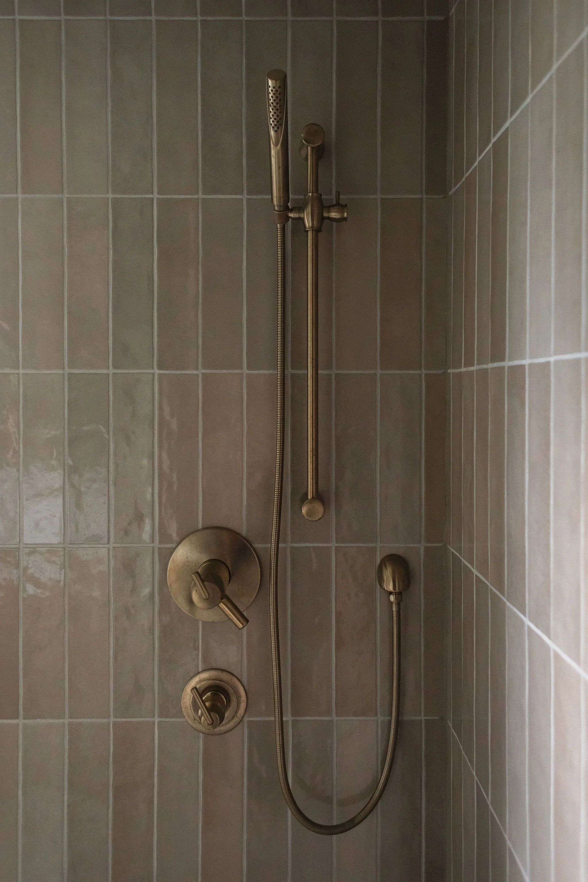 Close-up of aged brass shower fixtures against vertical taupe tile in a thoughtfully designed Edmonton bathroom.