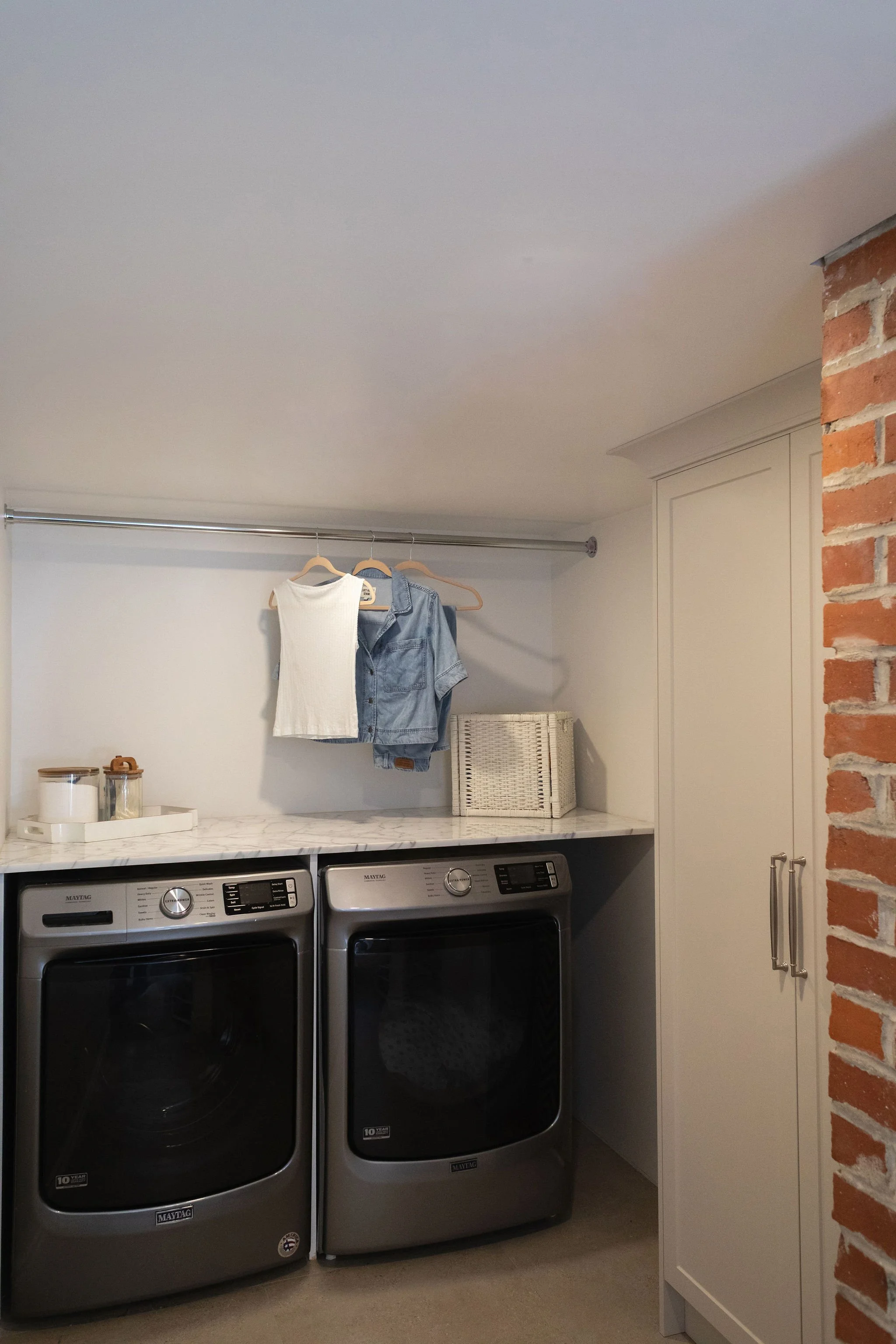 Laundry room remodel featuring front-load washer and dryer, marble folding counter, hanging rail and tall beige storage cabinetry.