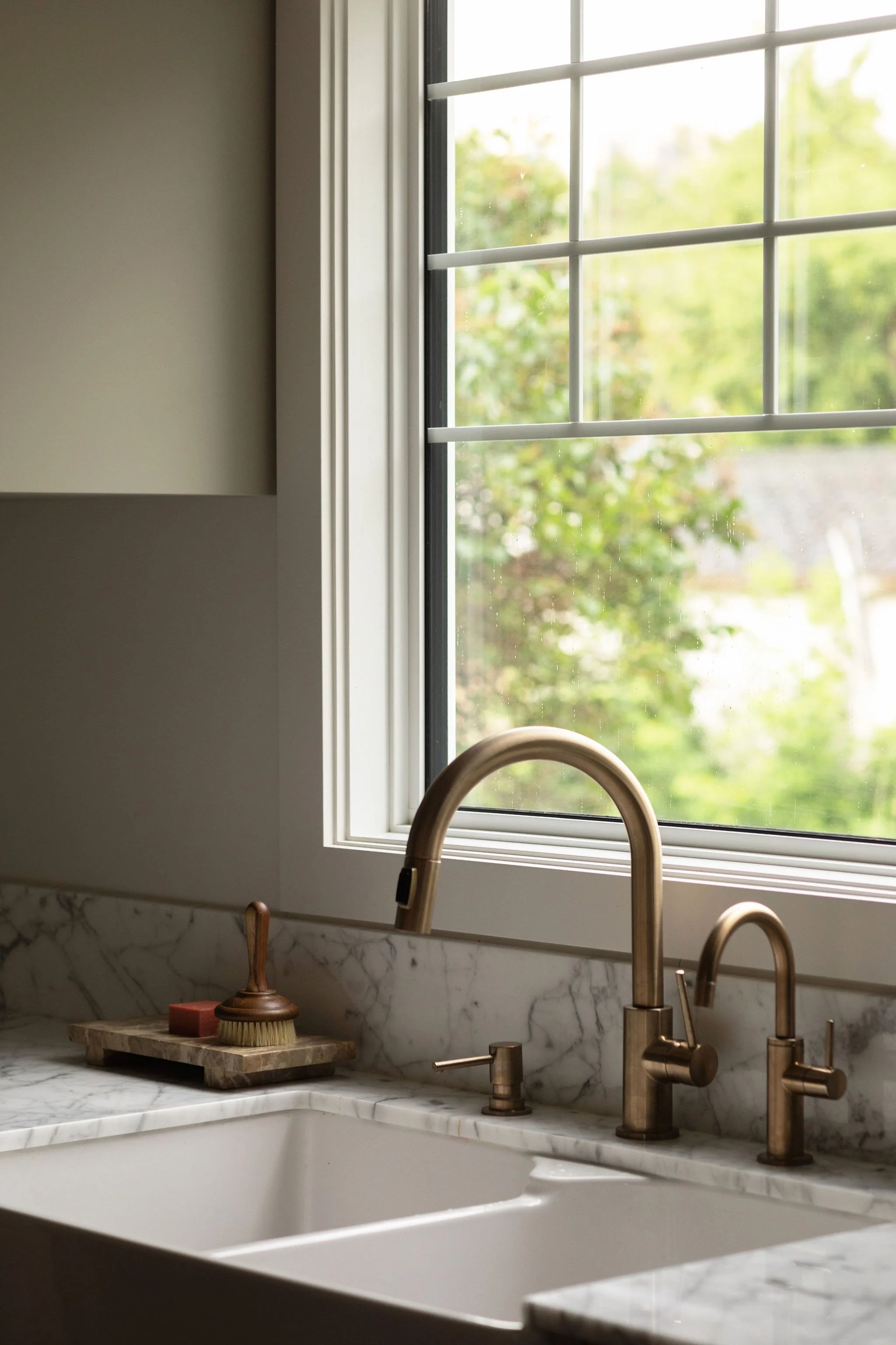 Close-up of a farmhouse kitchen sink with aged brass fixtures and Gioia marble countertops in The Bell renovation.