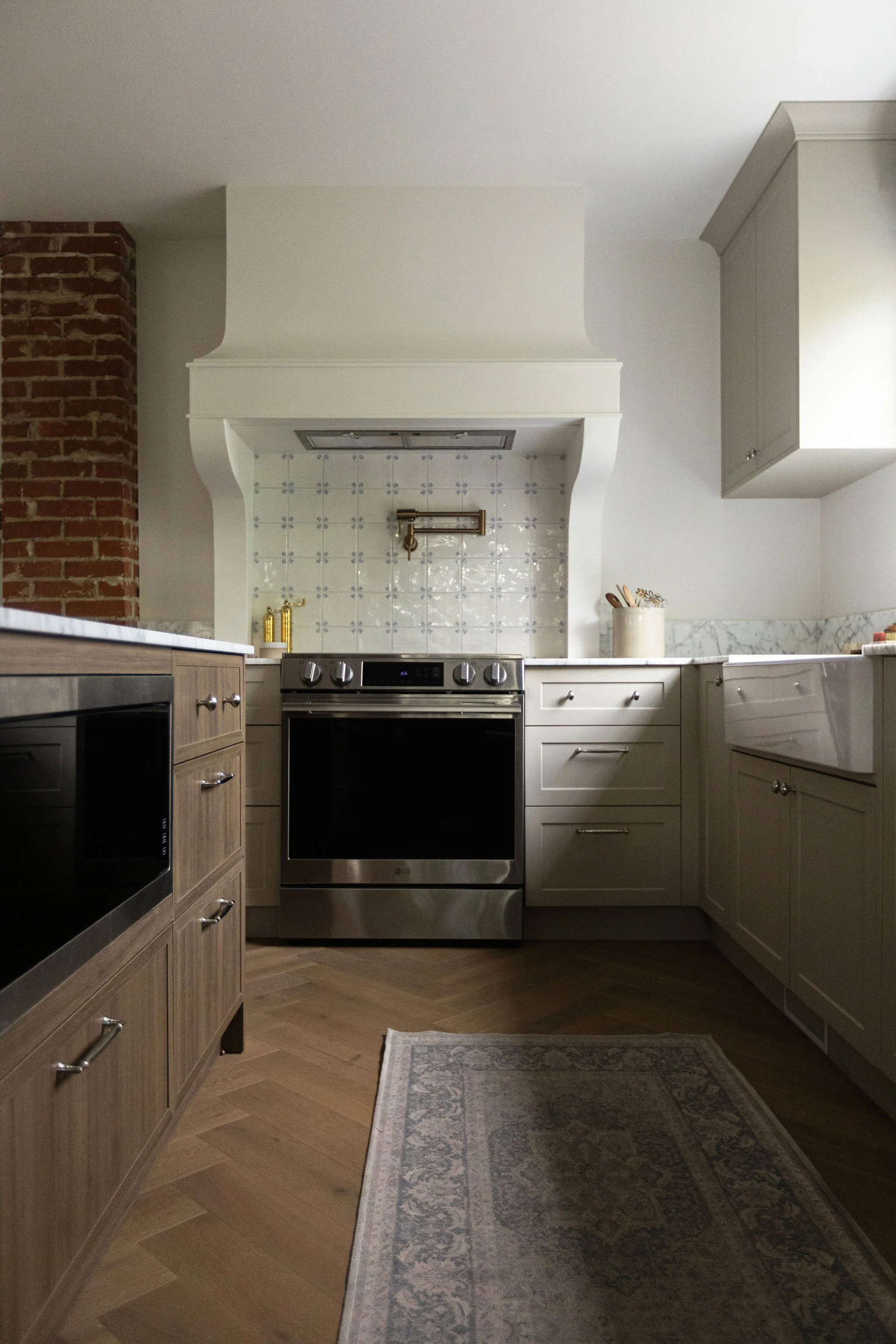 Custom kitchen range hood with Delft-inspired backsplash tile, beige cabinets and marble countertops in an Edmonton cottage renovation.