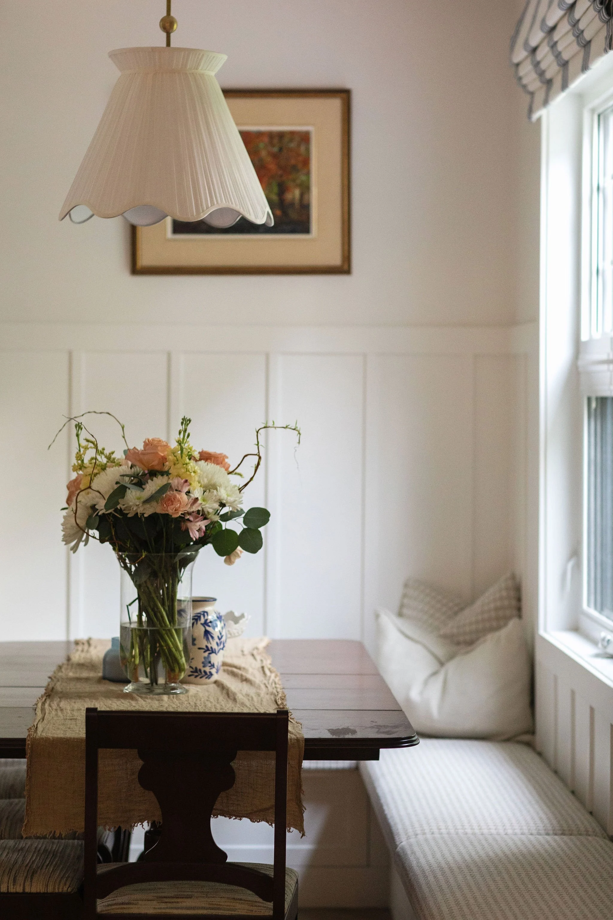 Cottage-style dining nook with a dark wood table, upholstered built-in bench and decorative pendant lighting.