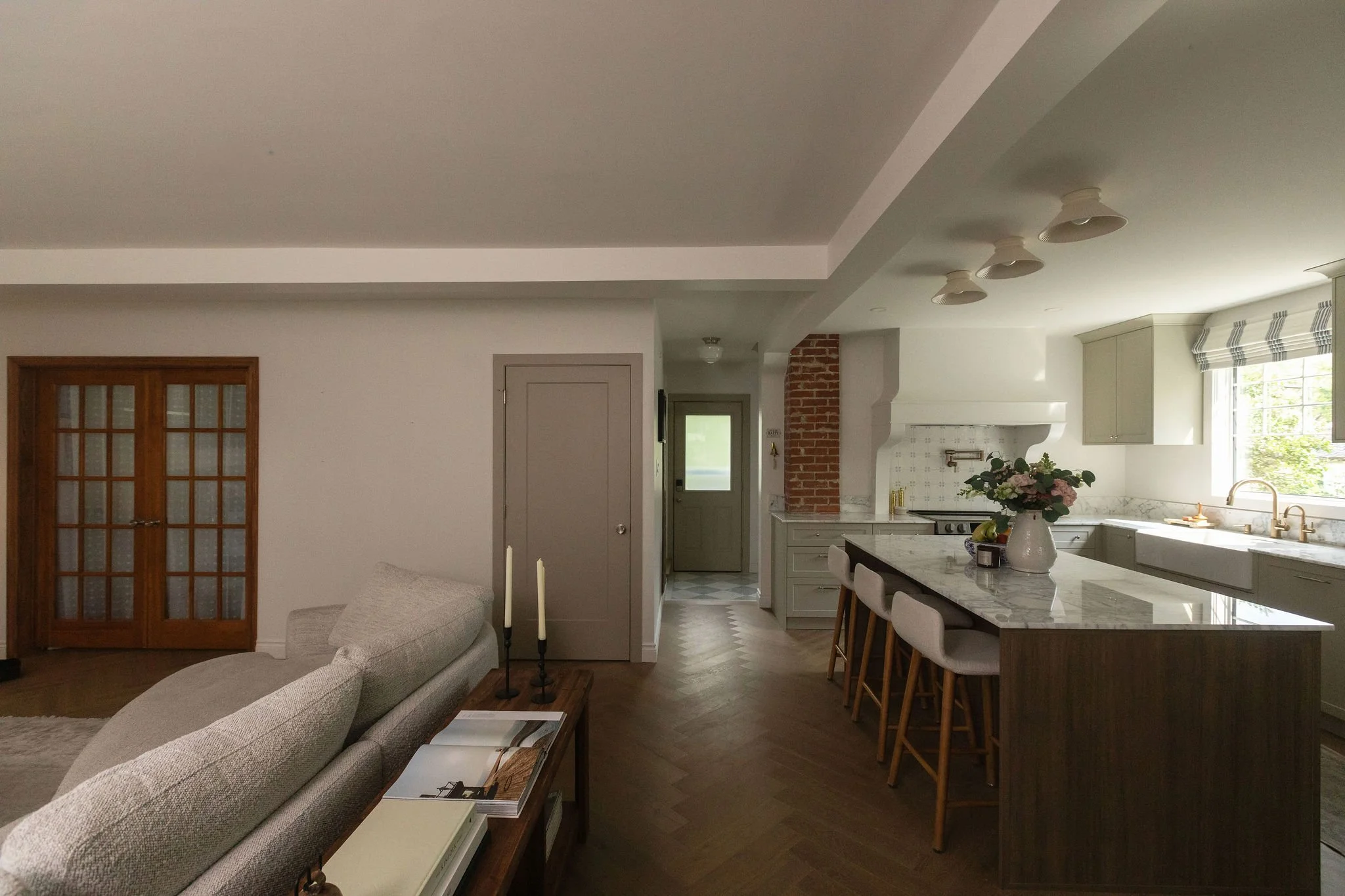 Open-concept kitchen and living room with a dark wood island, beige cabinets and original-style French doors.