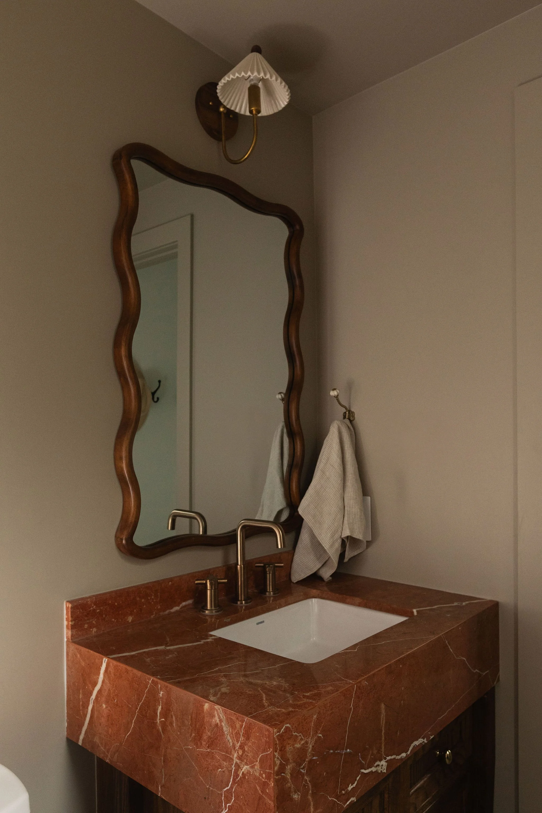 Vintage-inspired bathroom vanity with a bold red marble countertop, sculptural wood-framed mirror and brass plumbing fixtures.
