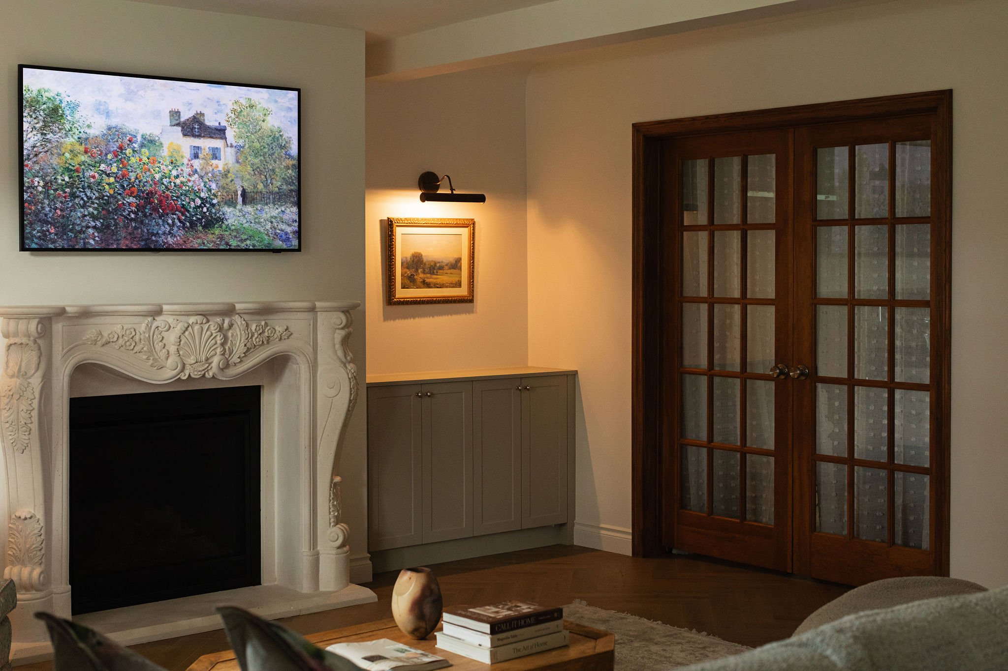 Traditional living room with dark wood French doors, a decorative fireplace surround and custom sage-green cabinetry.