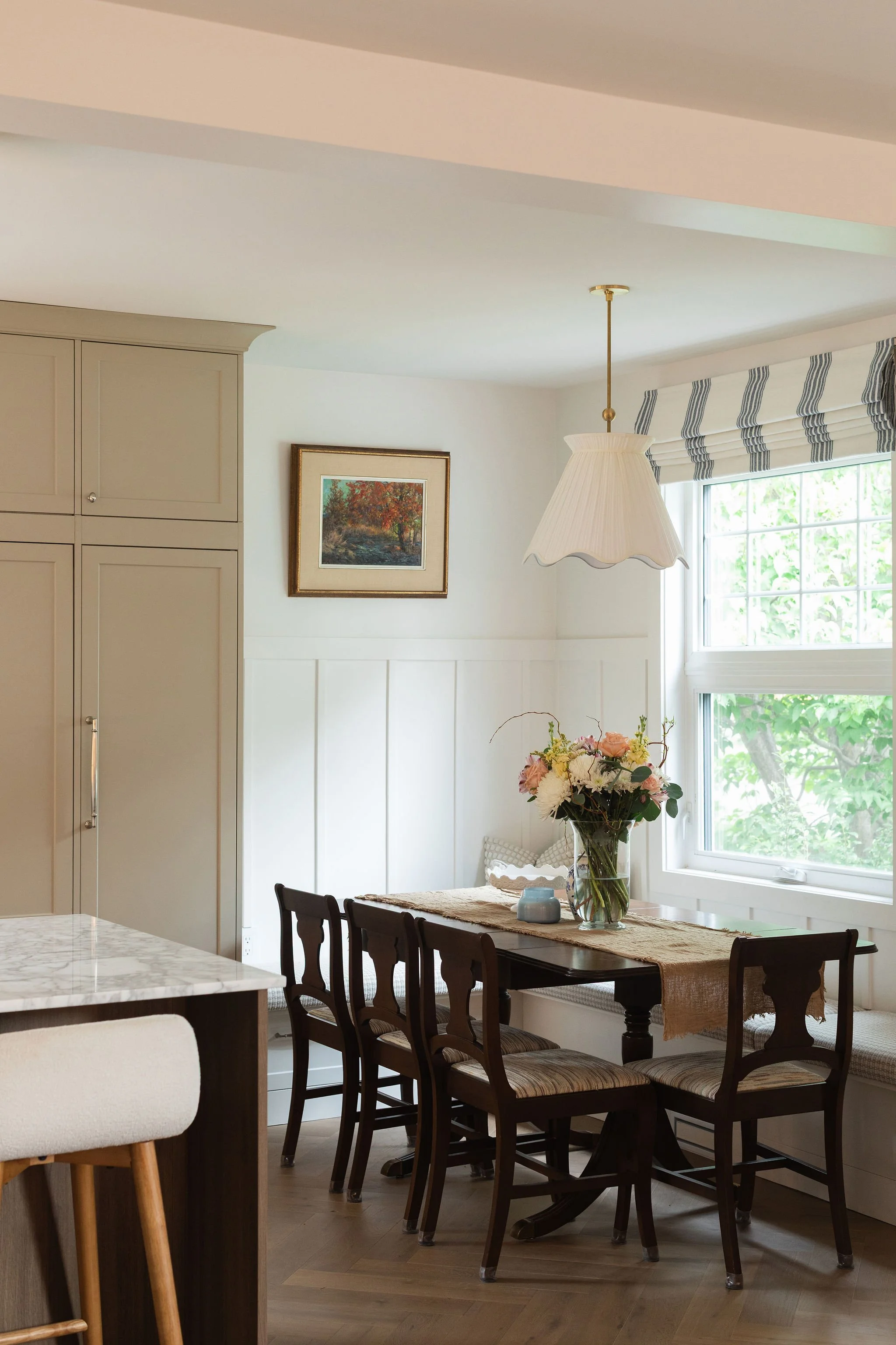Dining nook in The Bell renovation featuring a dark wood table, built-in banquette seating and a scalloped pendant light.