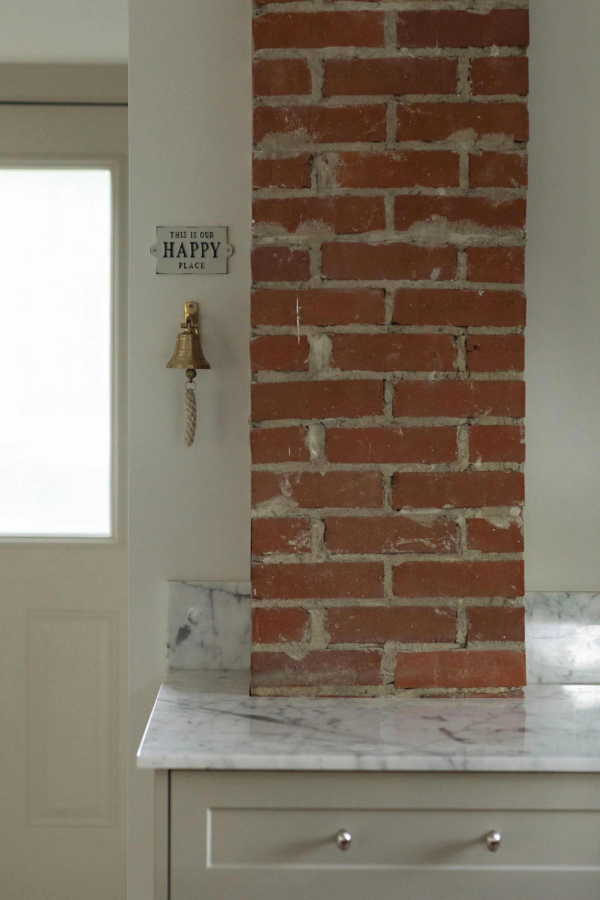 Exposed red brick chimney beside custom kitchen cabinetry and marble countertops in a character-filled Edmonton home.