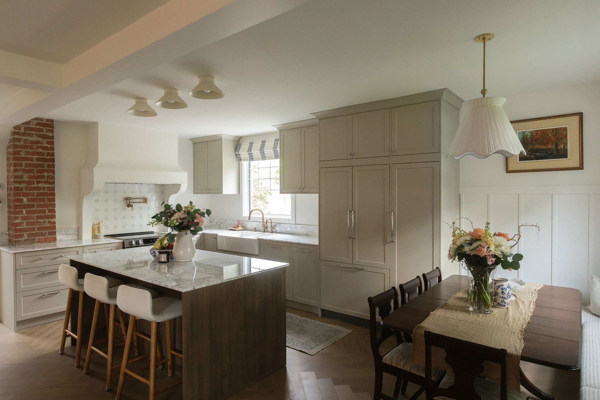 Kitchen and dining room renovation featuring a dark wood island, beige cabinetry, marble countertops and classic cottage details.