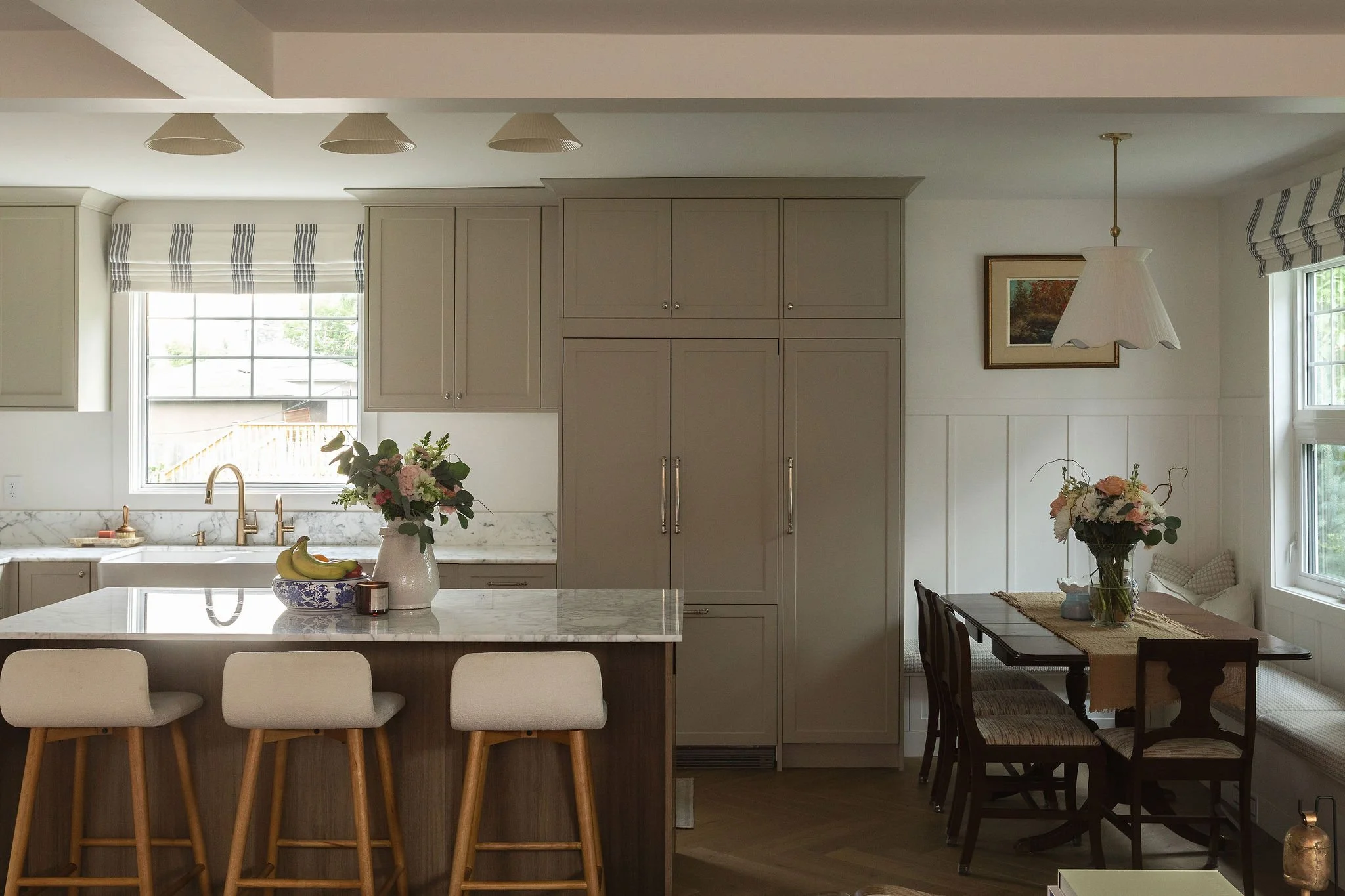 Open kitchen and dining area with beige cabinetry, a dark wood island, marble countertops and built-in banquette seating.