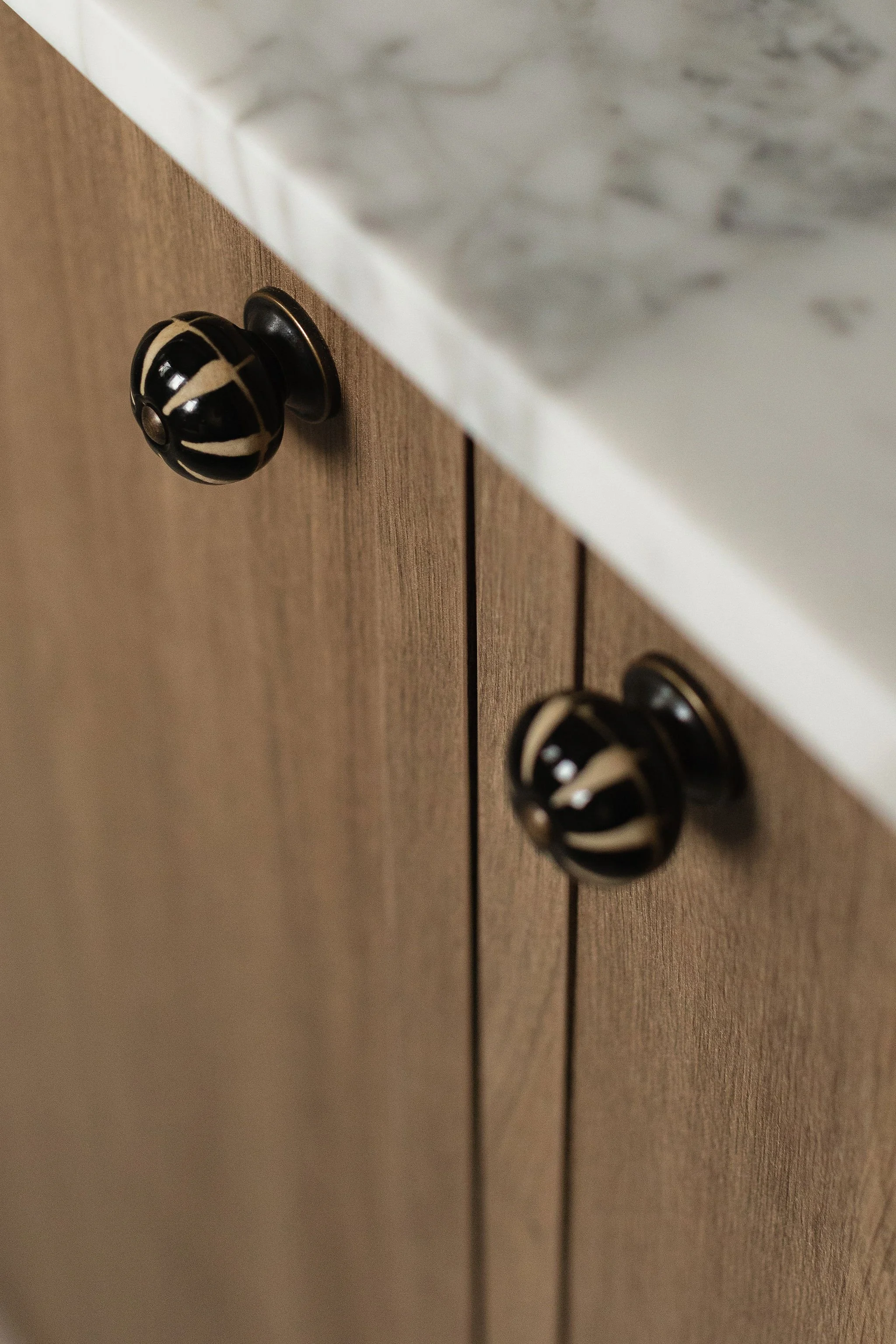 Close-up of decorative black and cream cabinet knobs on natural wood vanity cabinetry beneath a marble countertop.