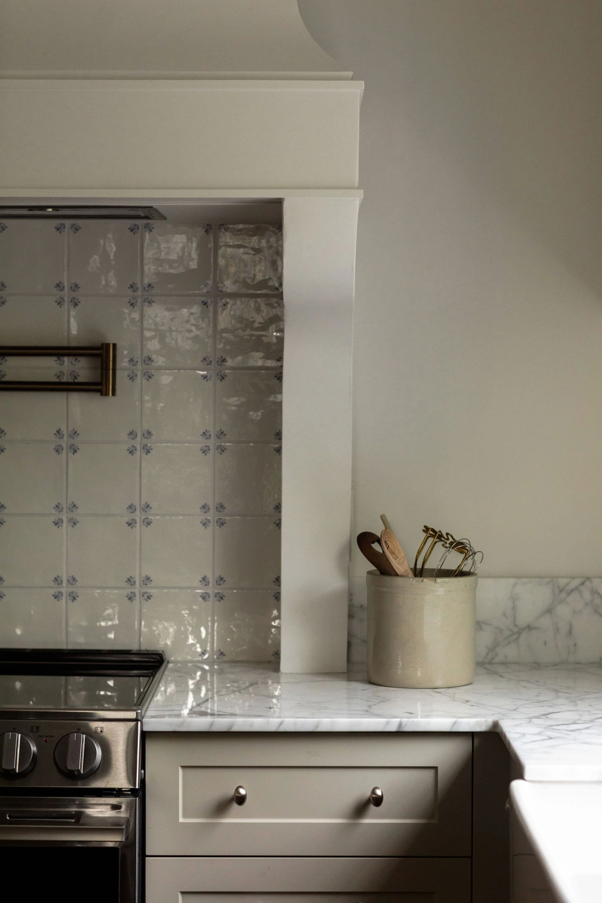 Custom white drywall range hood framing a Delft-inspired tile backsplash in a timeless Edmonton kitchen renovation.