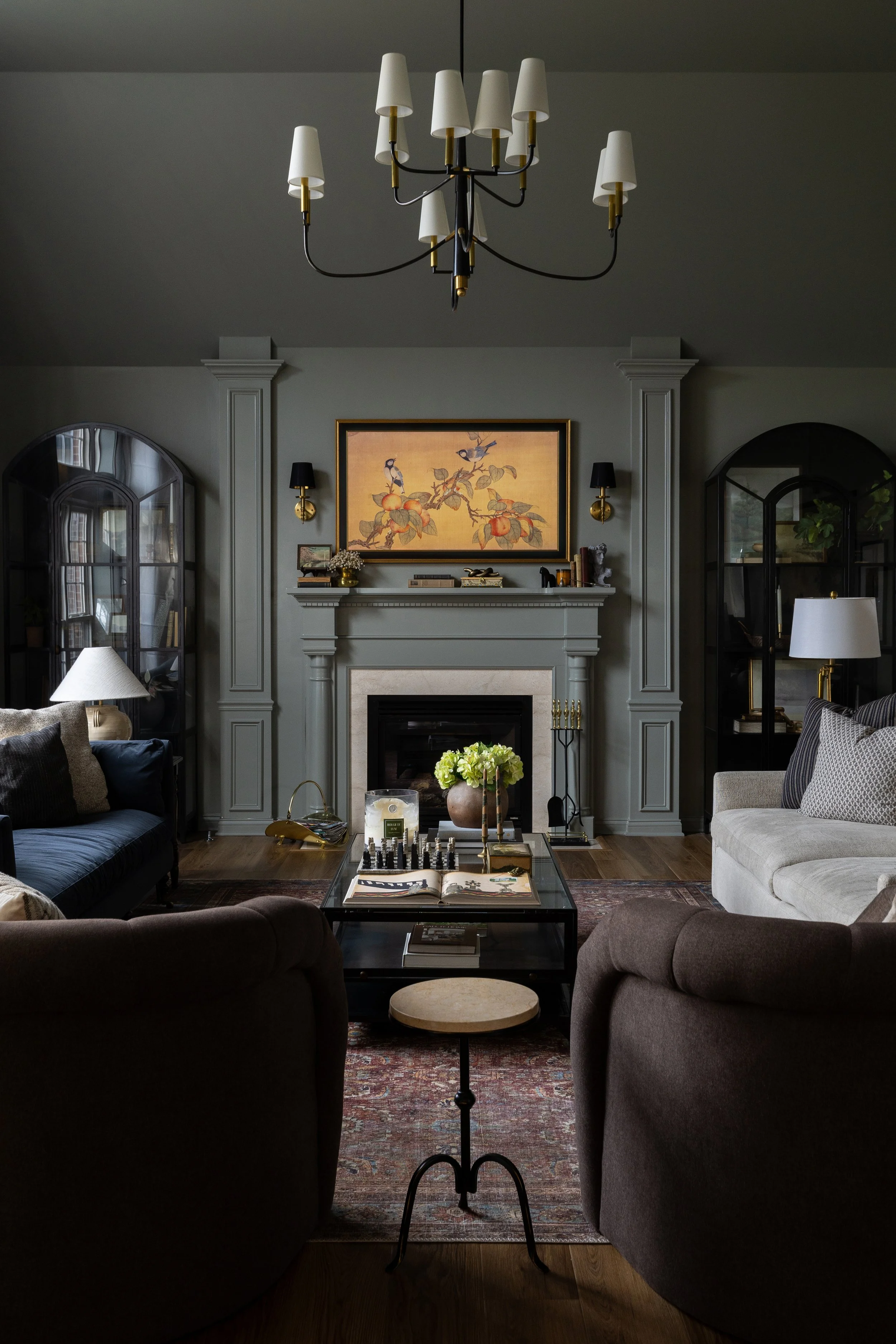 Elegant living room with a fireplace, artwork above, and various furniture and decor including armchairs, sofas, a chandelier, and shelves.
