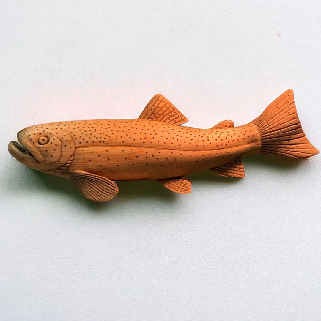 Wooden fish sculpture painted orange with black spots, detailed fins and gills, placed on white surface.