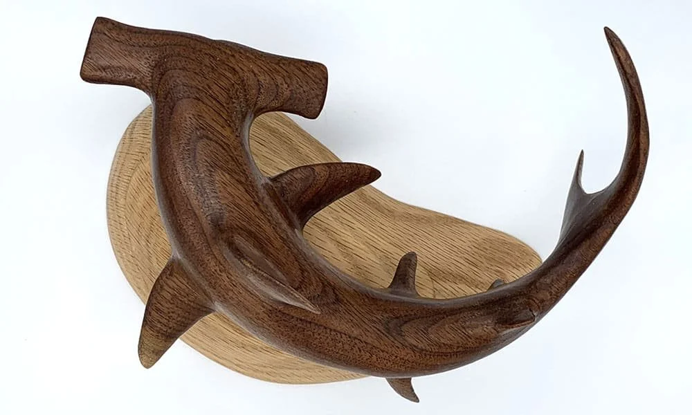Decorative wooden hammerhead shark sculpture mounted on a wooden base.