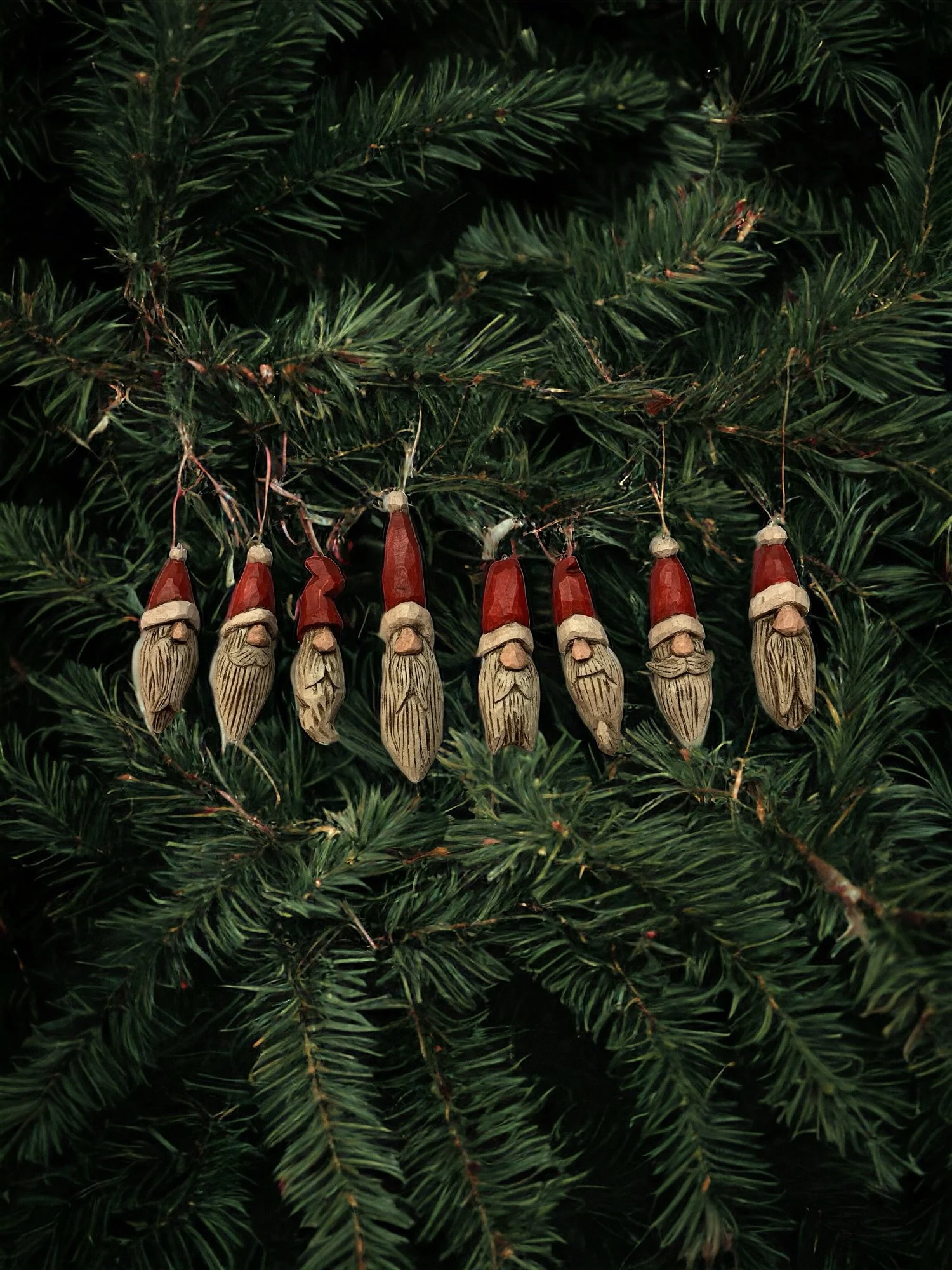 A string of vintage wooden Santa Claus ornaments hanging on a Christmas tree with green pine needles.