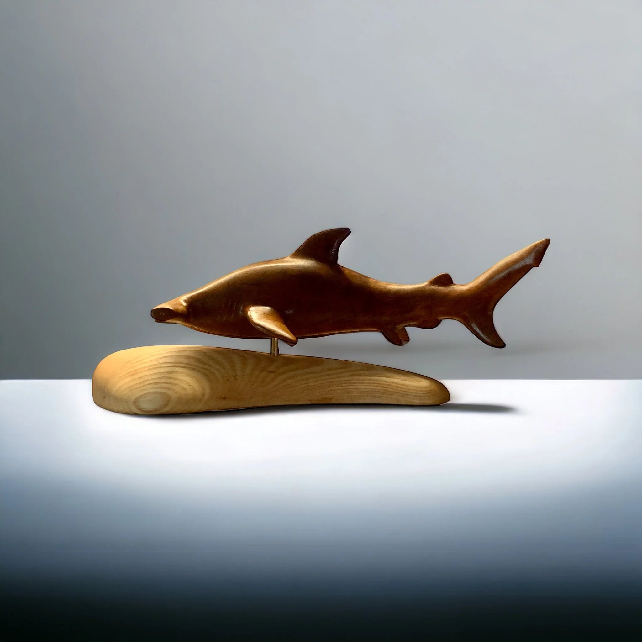 Wooden hammerhead shark sculpture on a wooden base, set against a plain gray background.