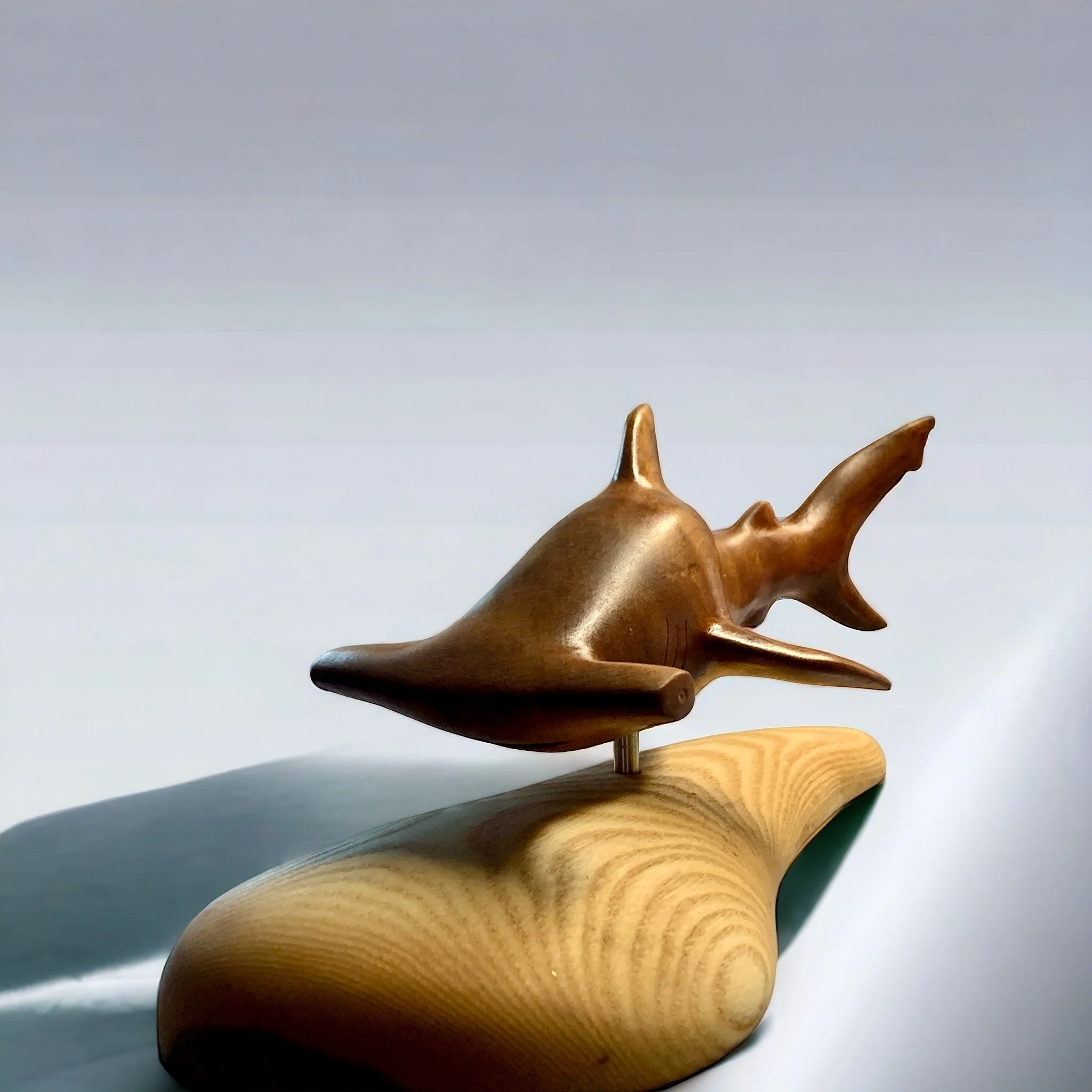 A wooden sculpture of a hanmerhead shark on a wooden base.