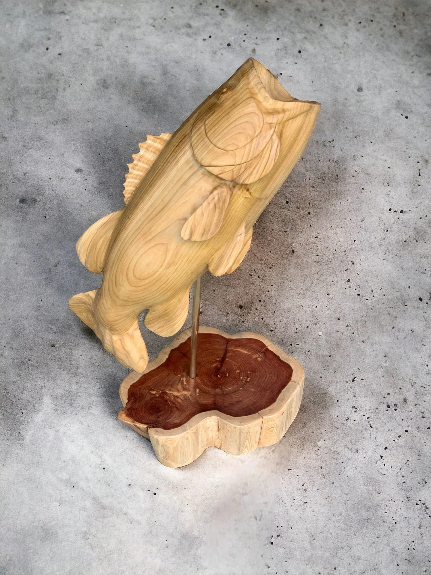 Wooden fish sculpture with a stand, placed on a concrete surface.