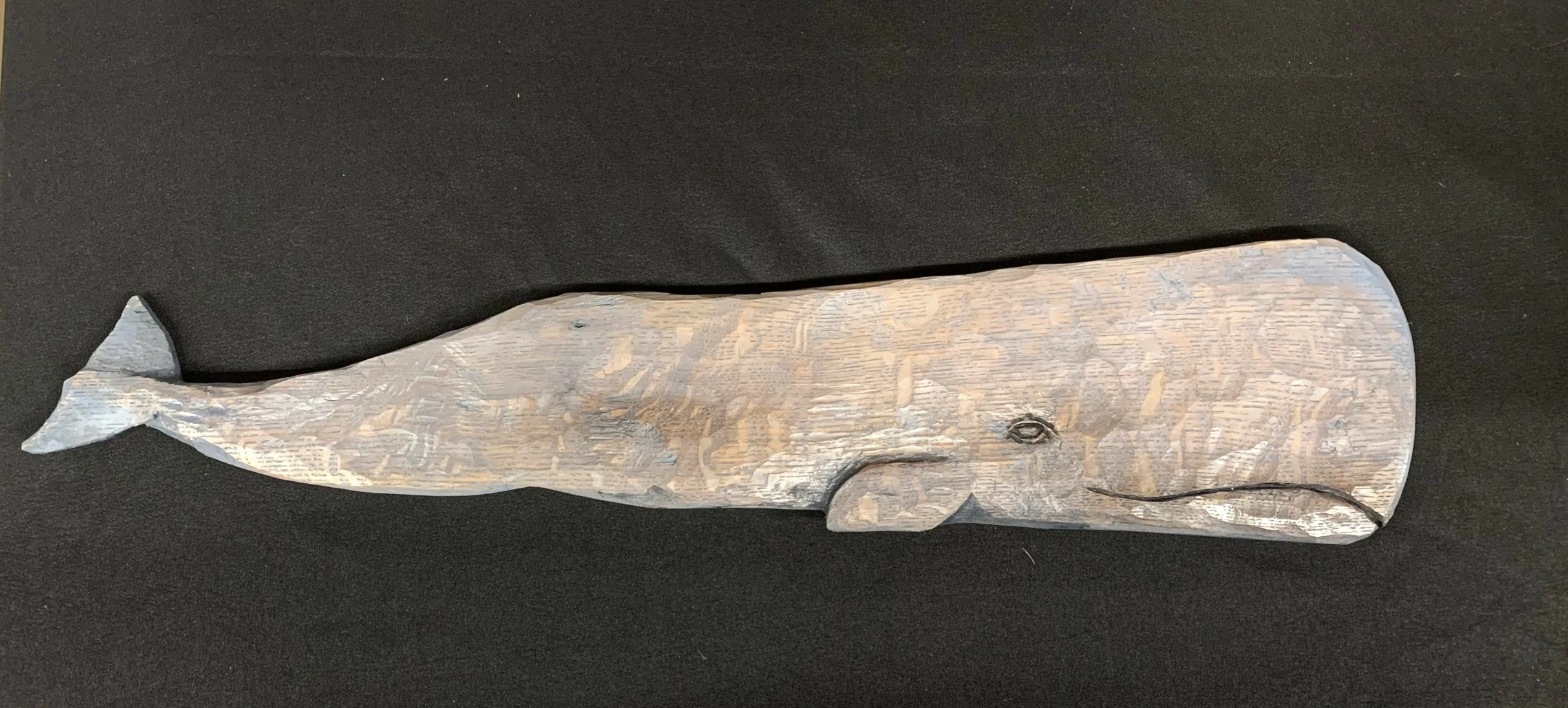 Wooden carving of a sperm whale on black background.