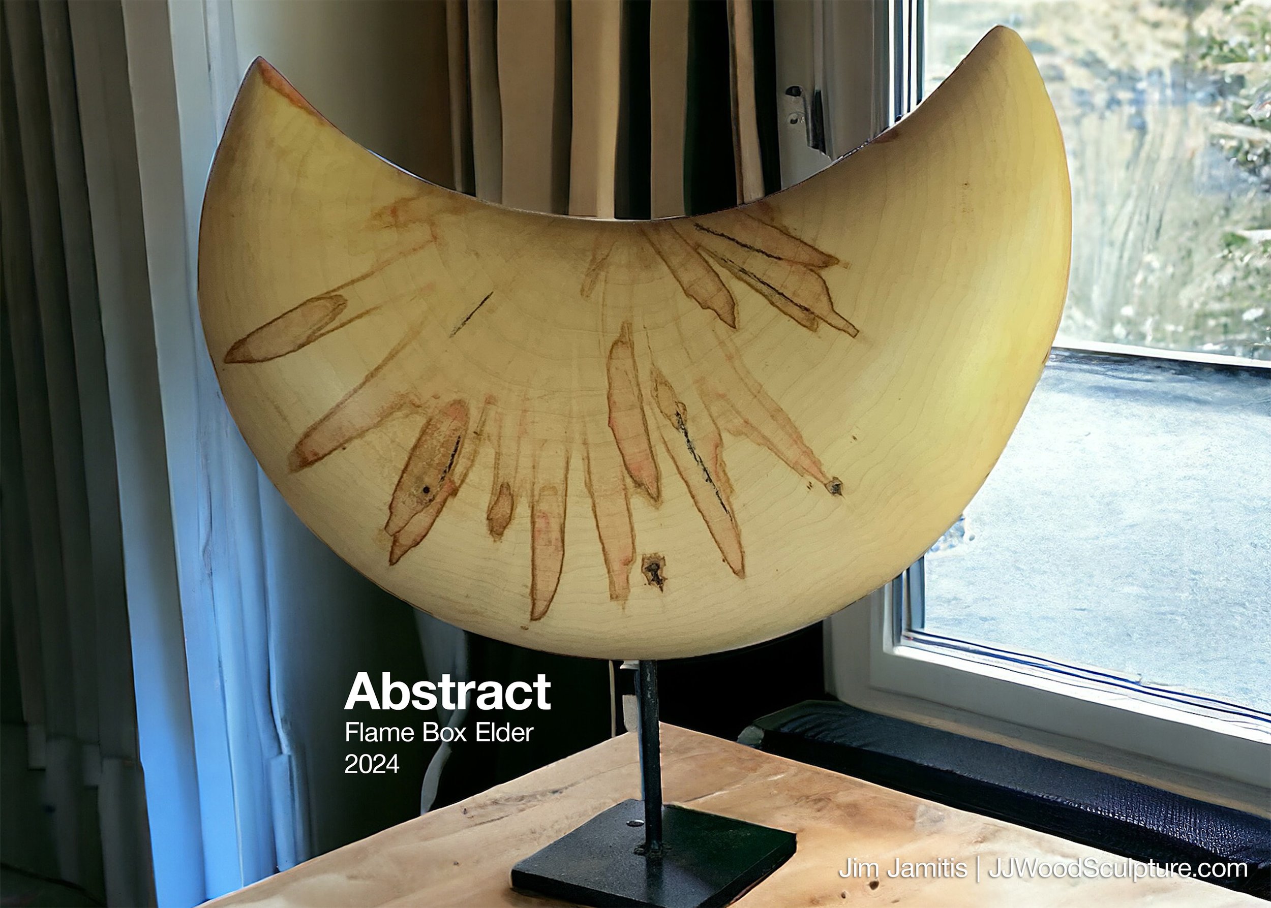 Wooden sculpture resembling a crescent moon with natural wood finish, mounted on a black metal stand near a window with greenery outside.