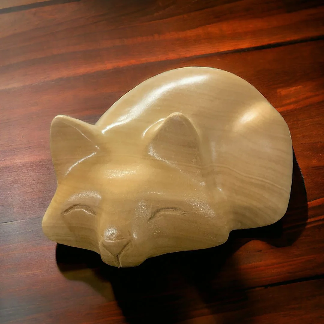 Wooden sculpture of a cat's face with closed eyes on a wooden surface.