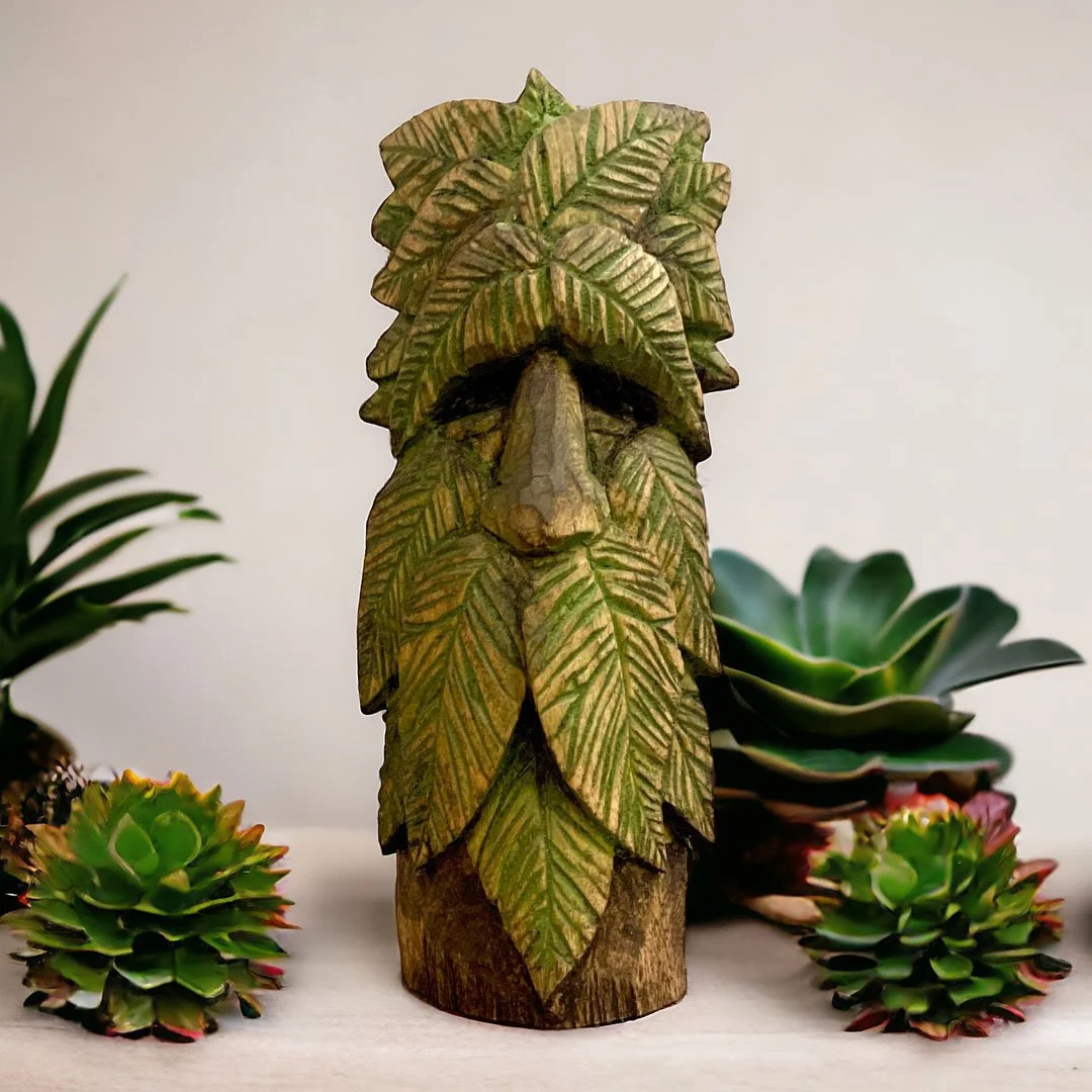 Wooden sculpture of a face with leaf-like features, surrounded by succulents and green plants.