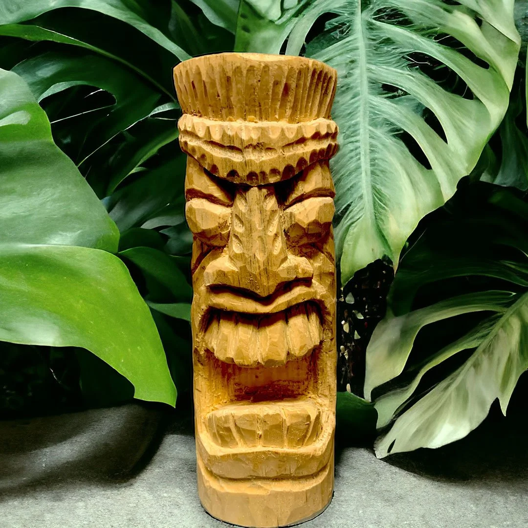 Wooden Tiki statue surrounded by green tropical leaves.