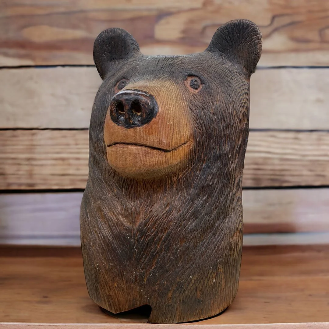 A carved wooden bear head sculpture with realistic features, set against a wooden background.