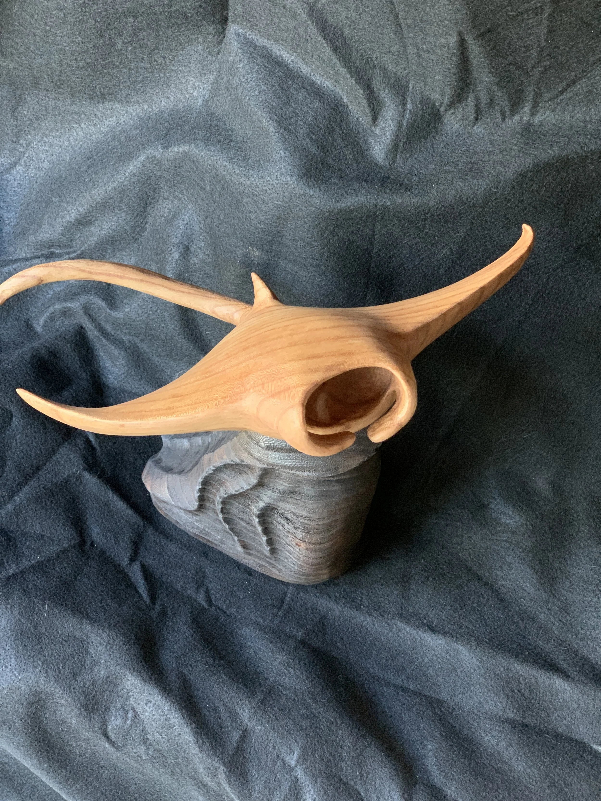 Wooden sculpture of manta ray, on a dark fabric background.