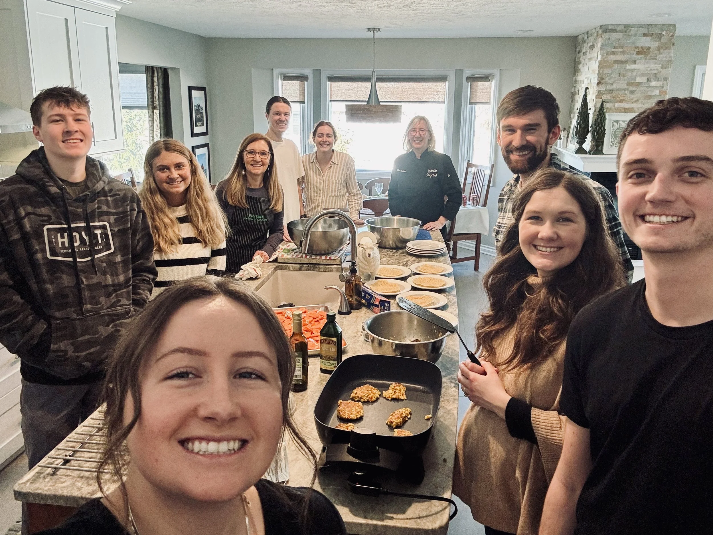 Group of people smiling while preparing food in a home kitchen.