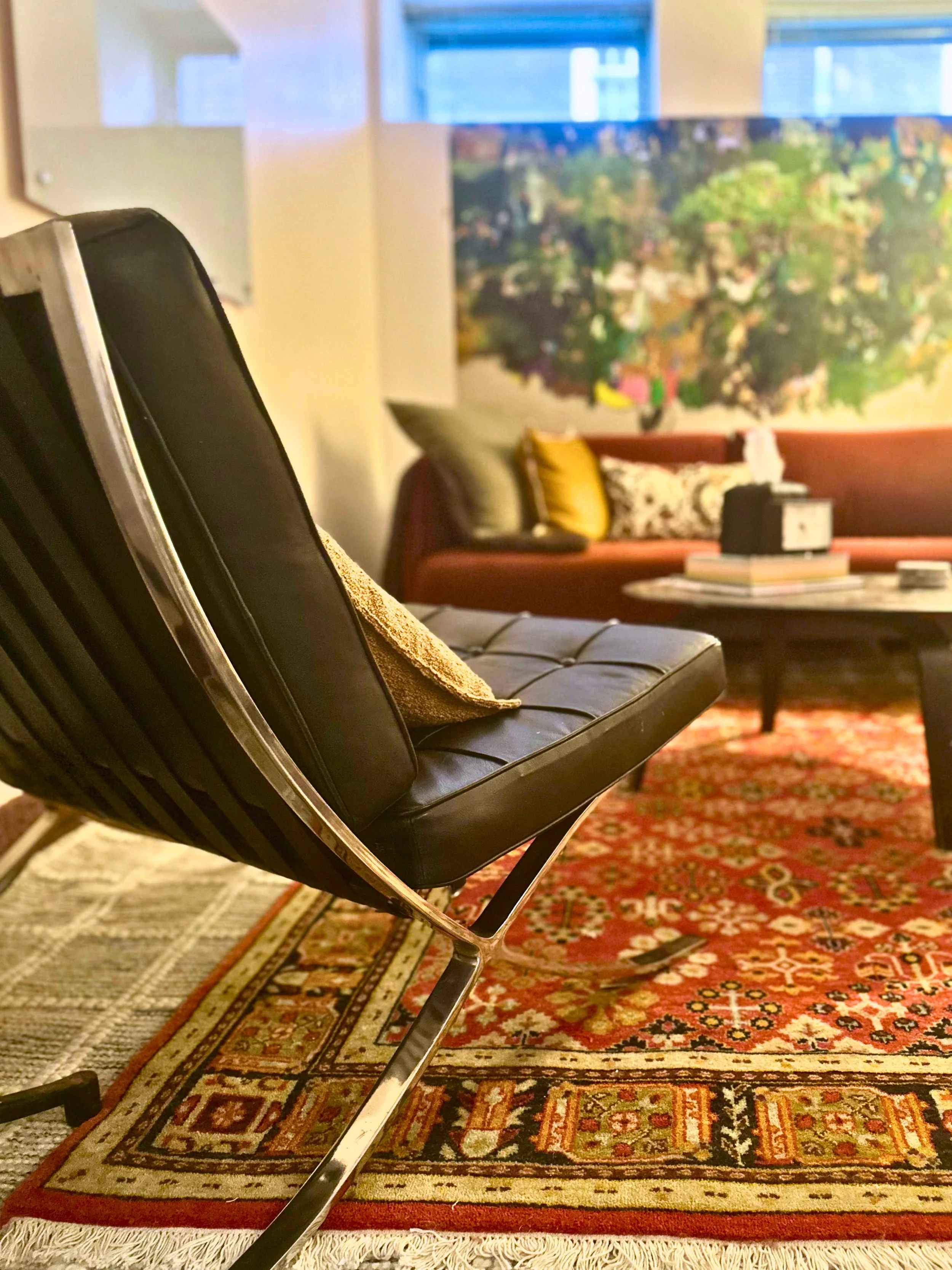 Therapy office featuring red patterned rug, black round table and back of black chair, with overall mid-century modern look