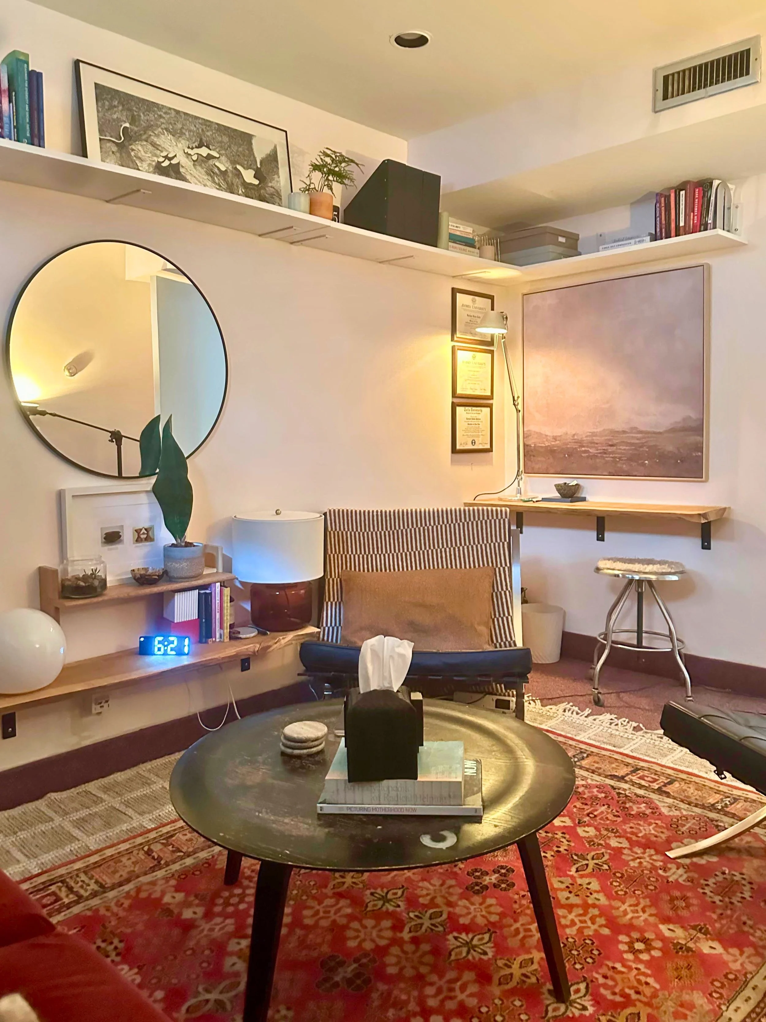 Therapy office featuring red patterned rug, black round table, with overall mid-century modern look