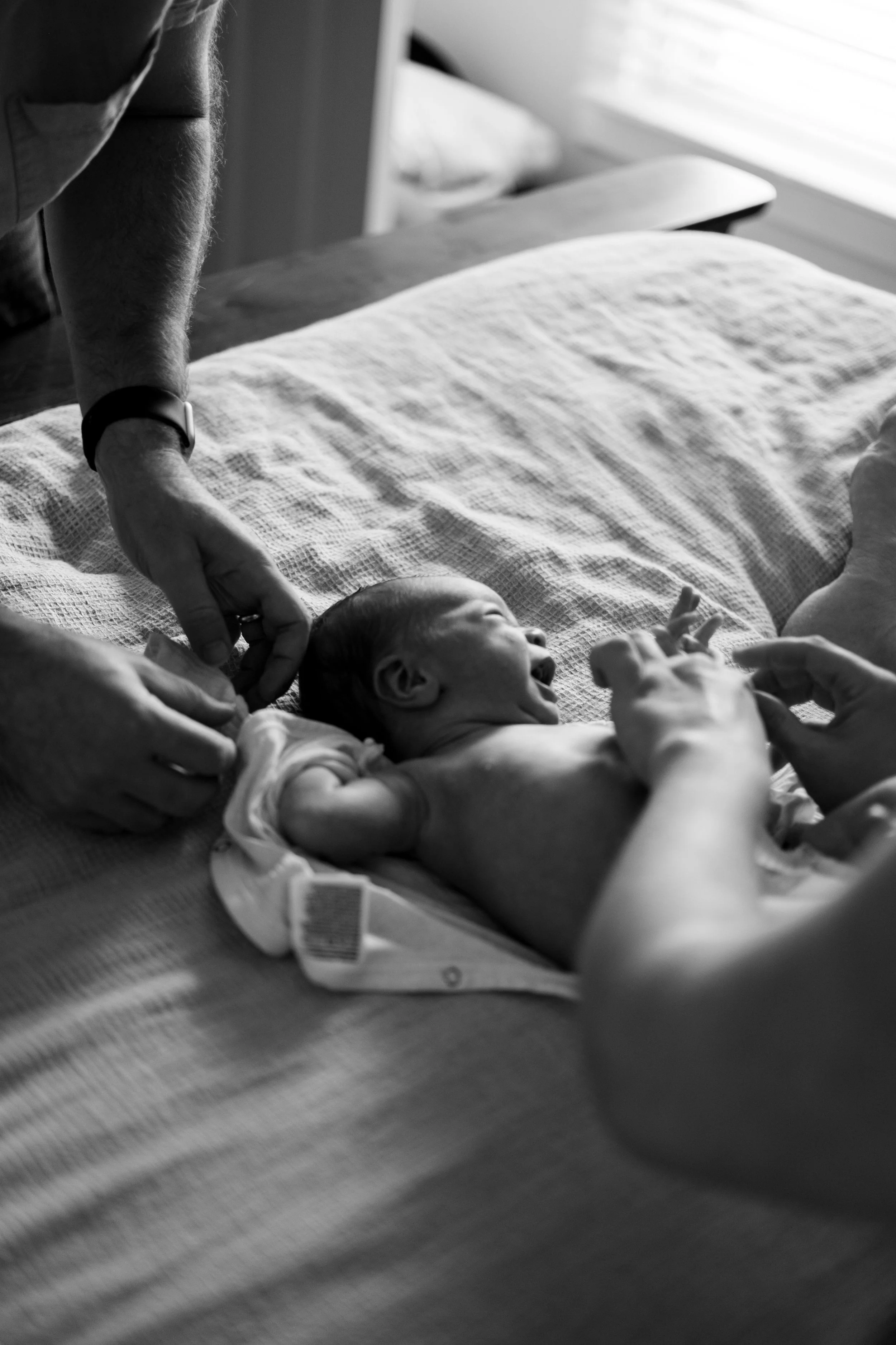 A newborn baby lying on a bed, with hands touching and the baby smiling, in a black and white photo.