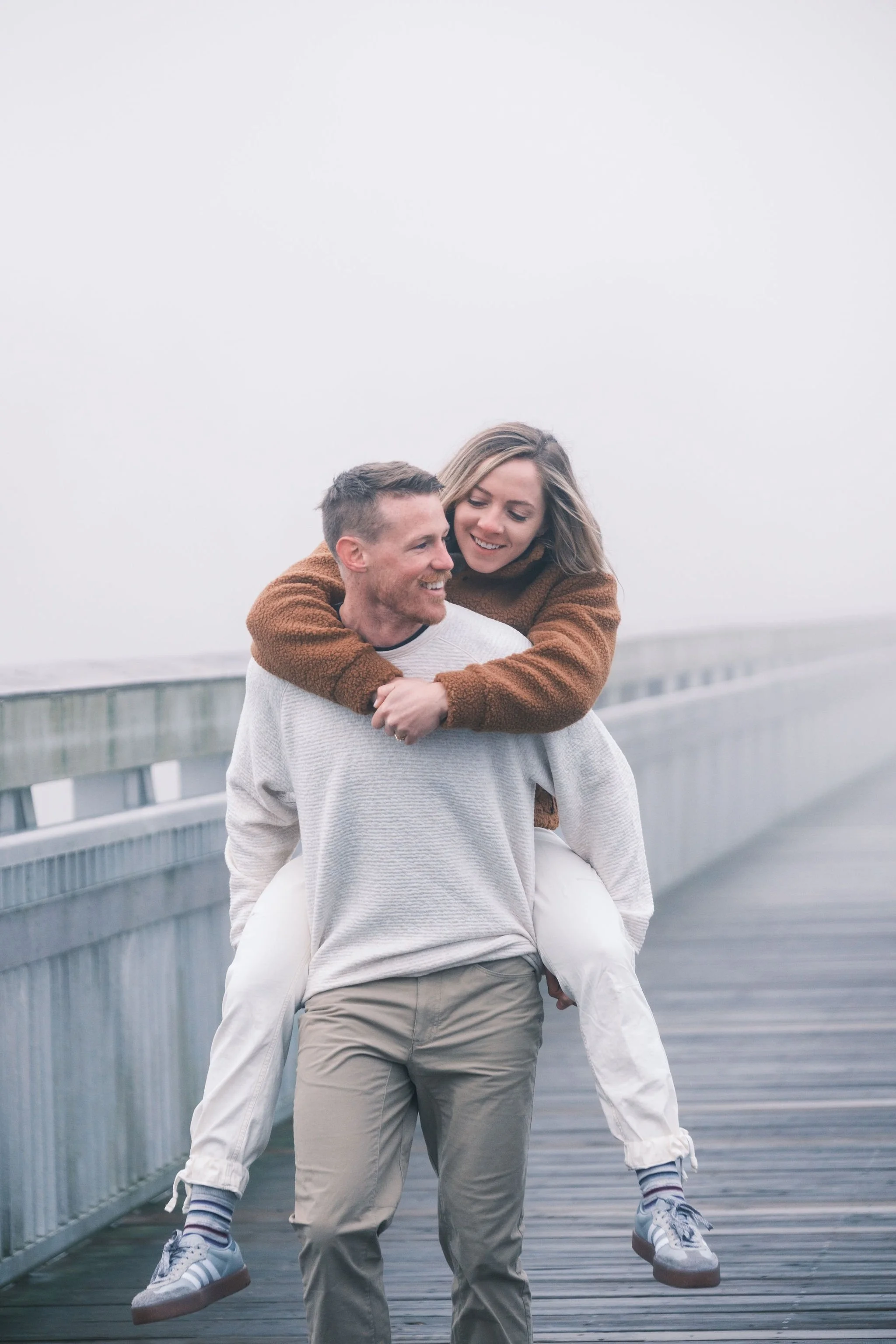 A couple with the woman on the man's back on a foggy wooden pier, smiling and enjoying each other's company.