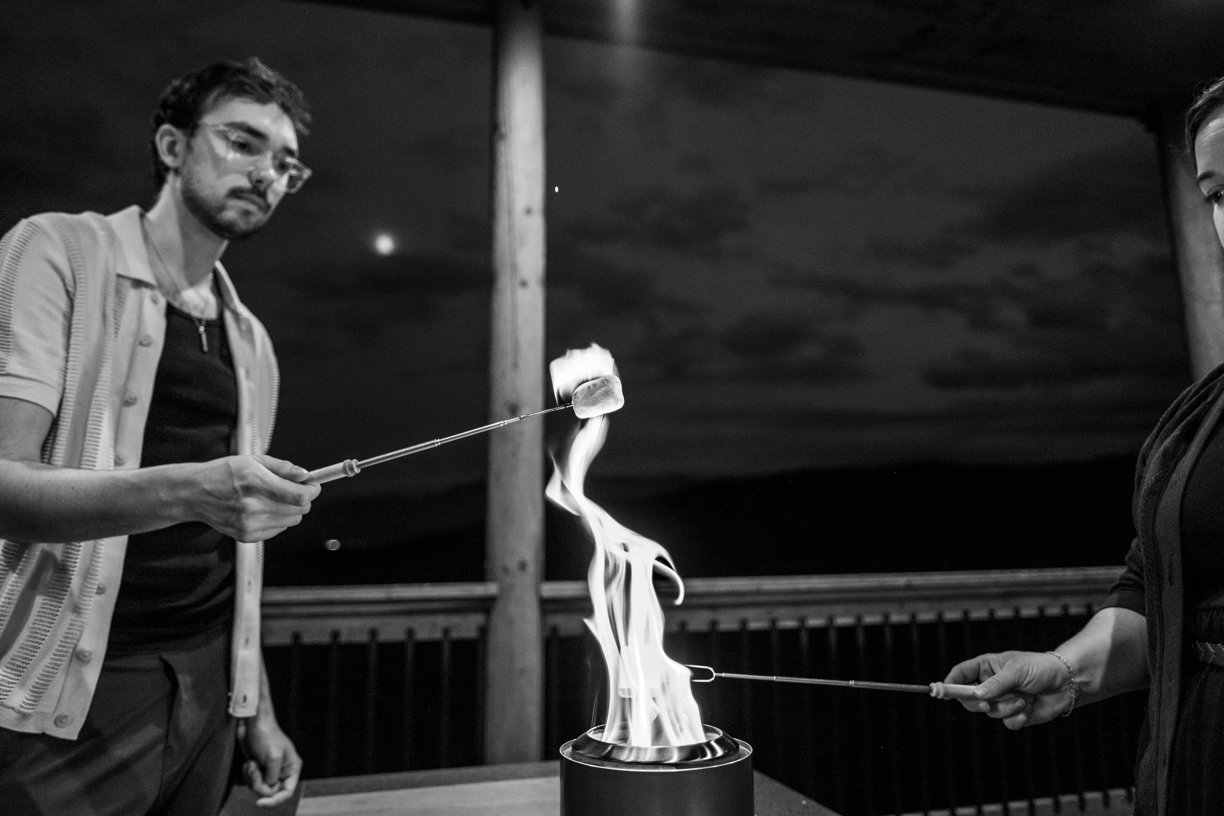 Two people roasting marshmallows over an outdoor fire pit at night.