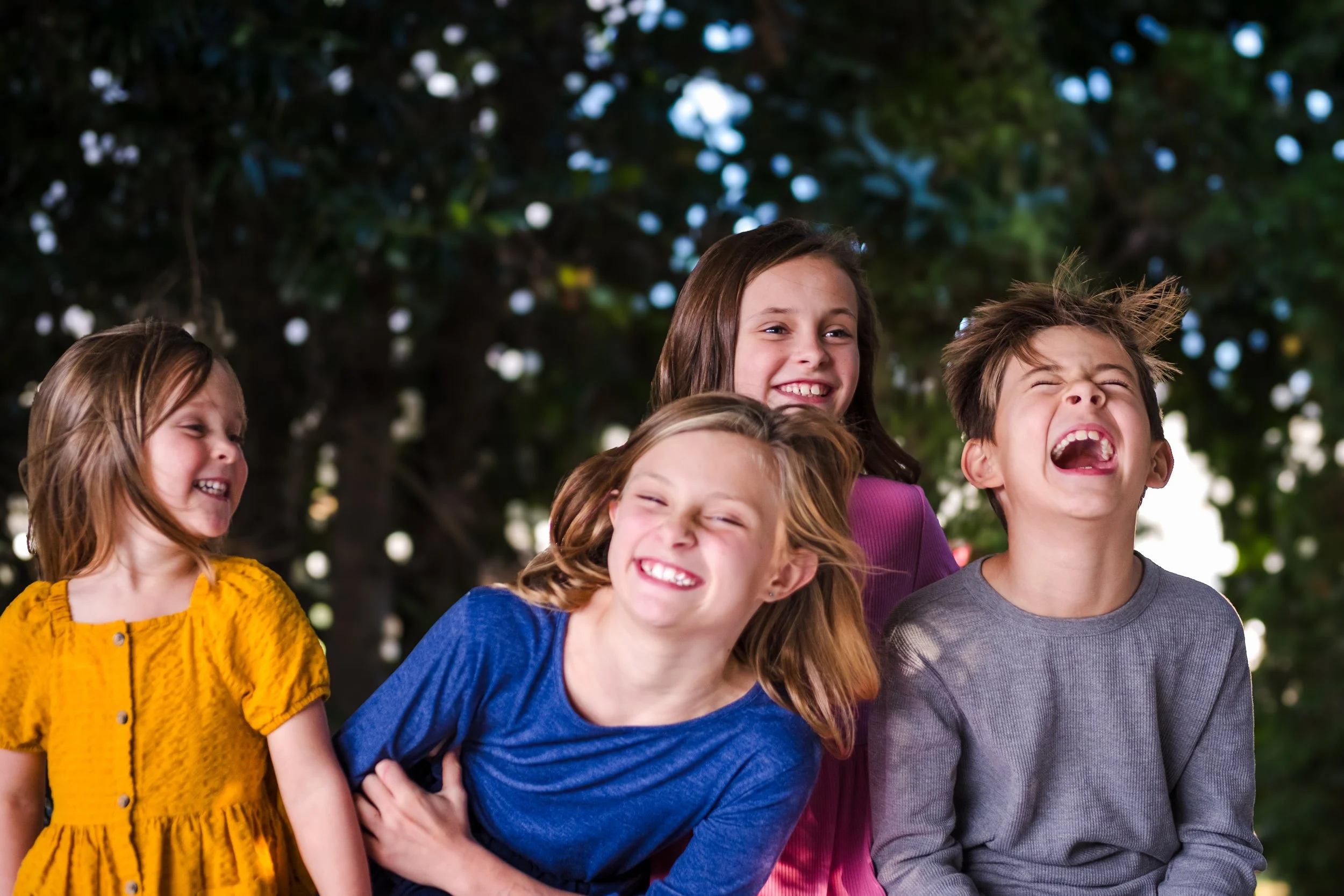 Group of five children laughing outdoors in front of trees.