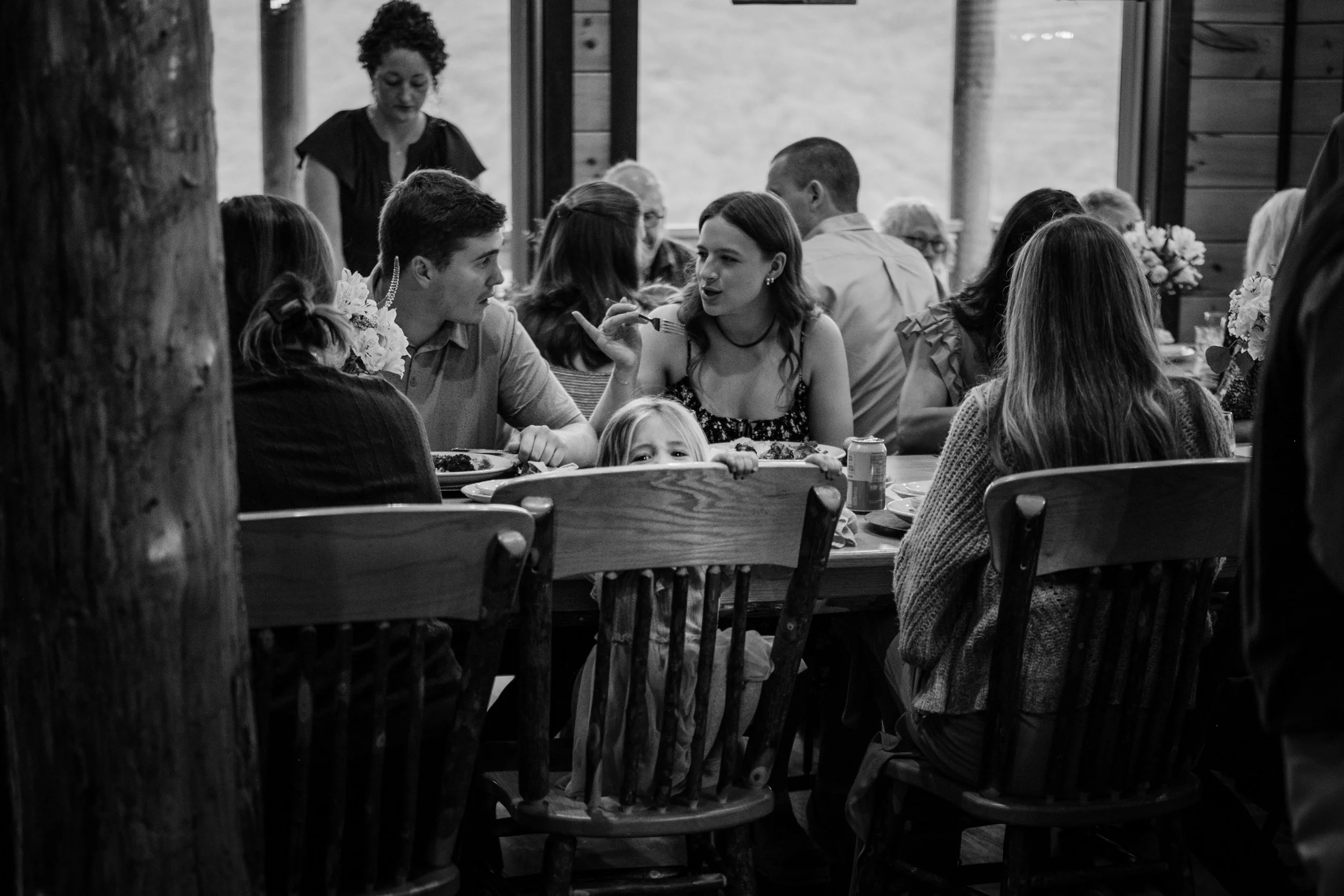 People sitting and eating at a large wooden table in a rustic restaurant, engaging in conversation.