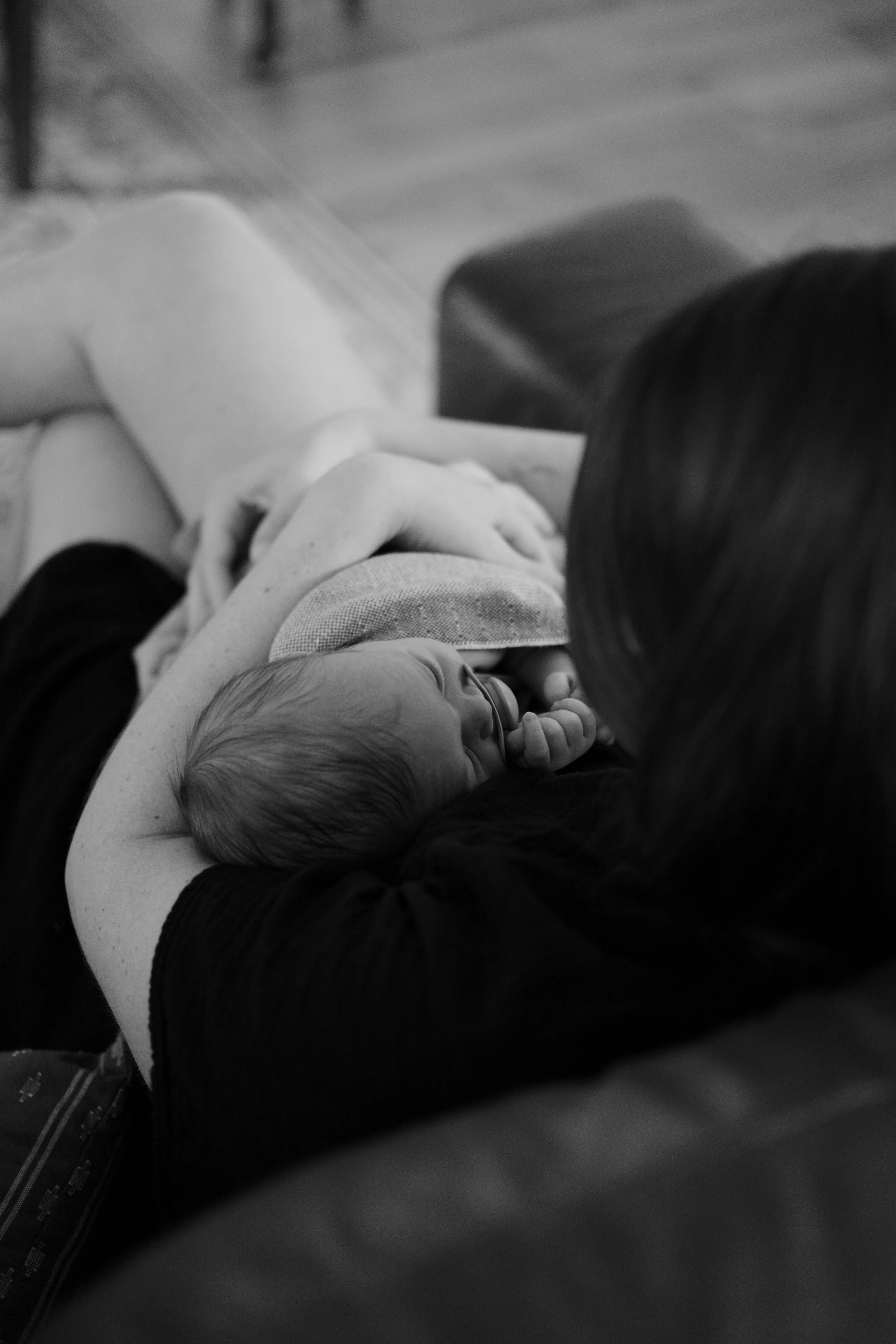 A person holding a newborn baby with a pacifier in the baby's mouth, lying on the person's arm.