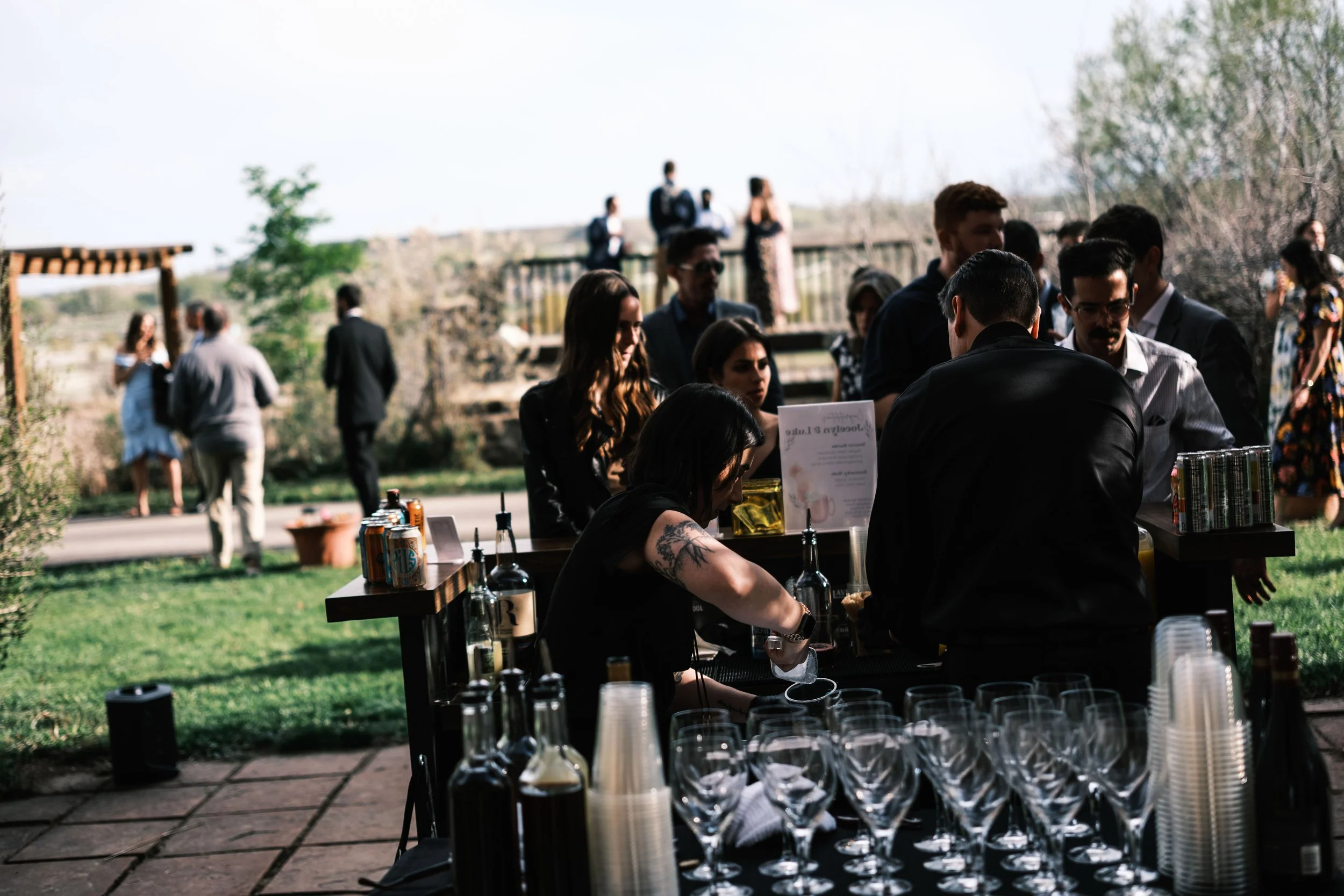 People gathering around a bar at an outdoor event on a sunny day.