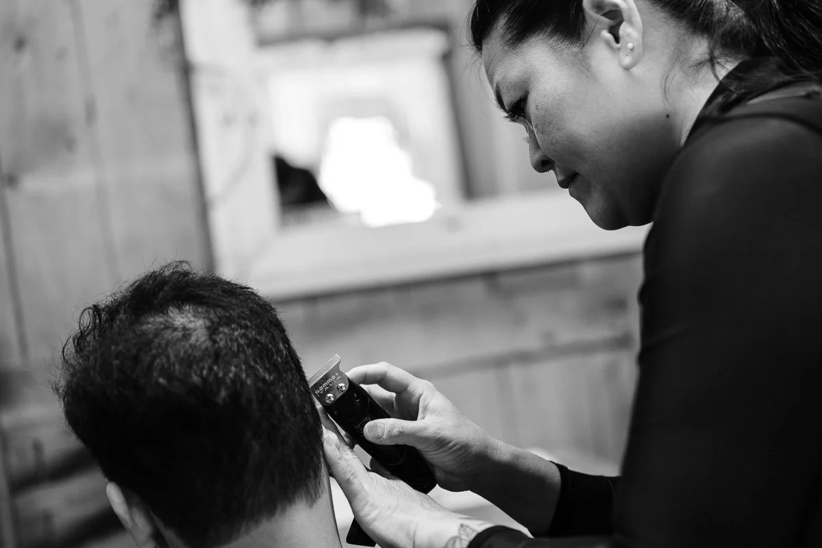 A woman cutting a man's hair with hair clippers in a salon or barbershop.