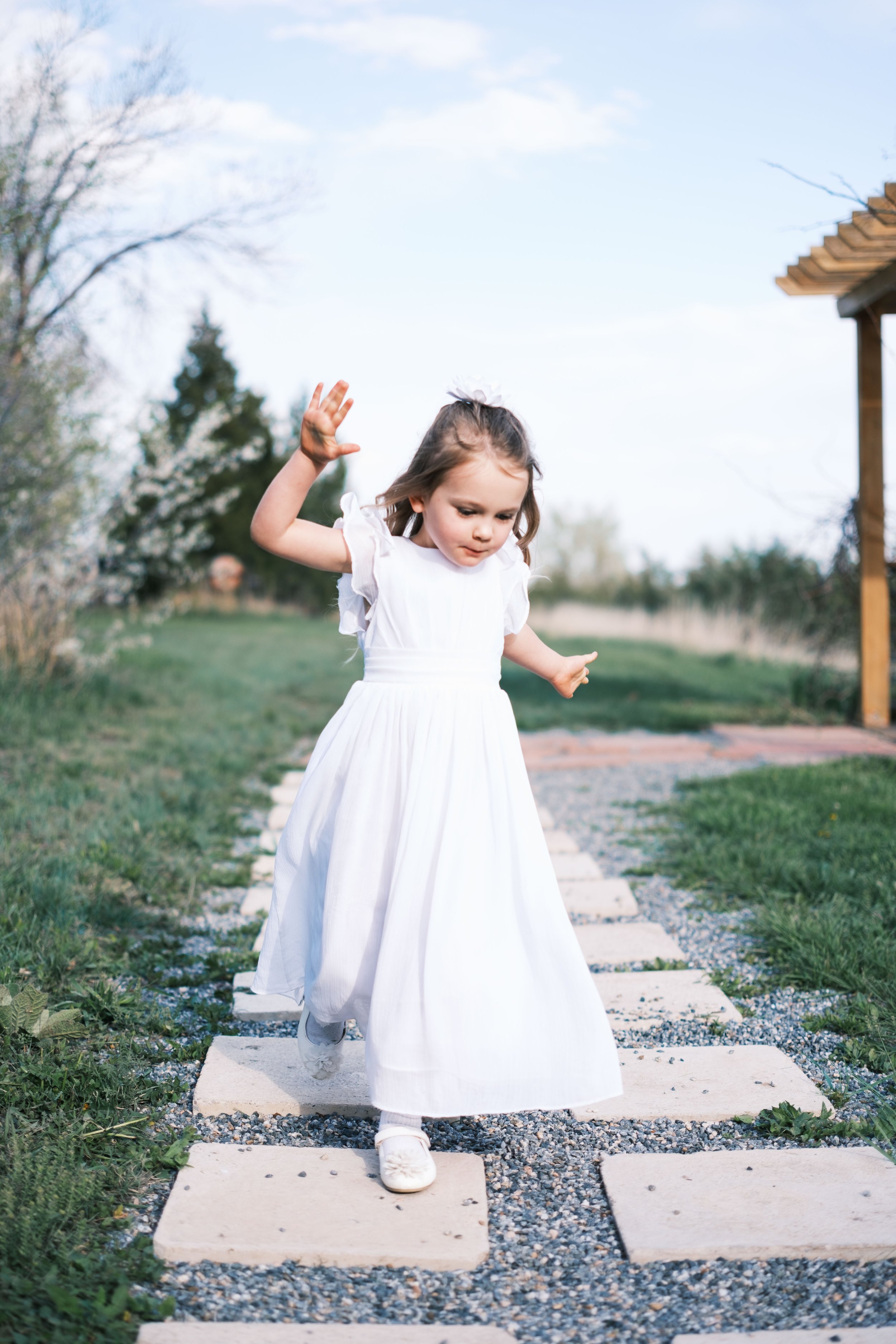 A young girl in a white dress walking on a stone pathway outdoors.