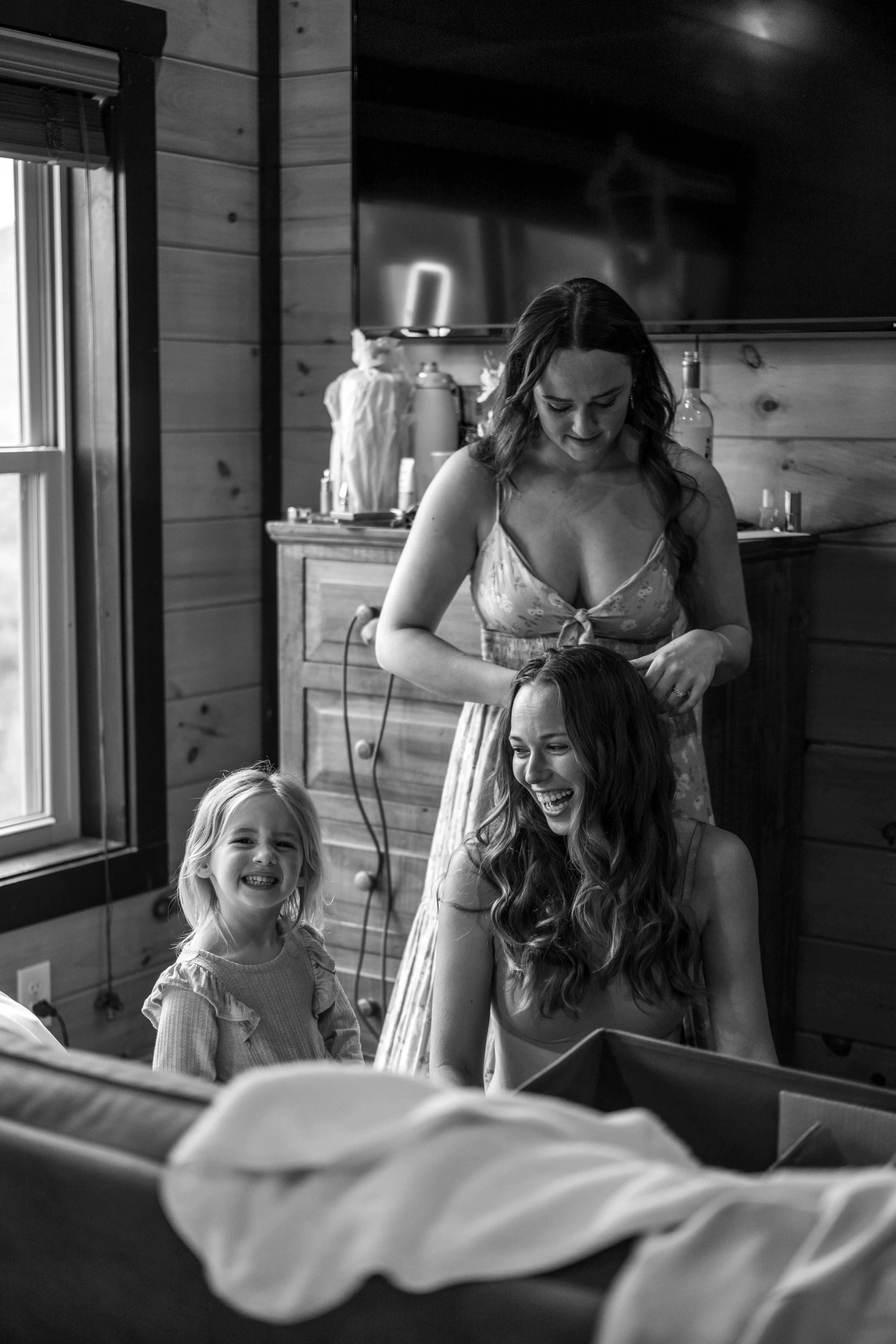 Three women and a young girl in a cozy, wooden room with natural lighting, laughing and enjoying a moment together.